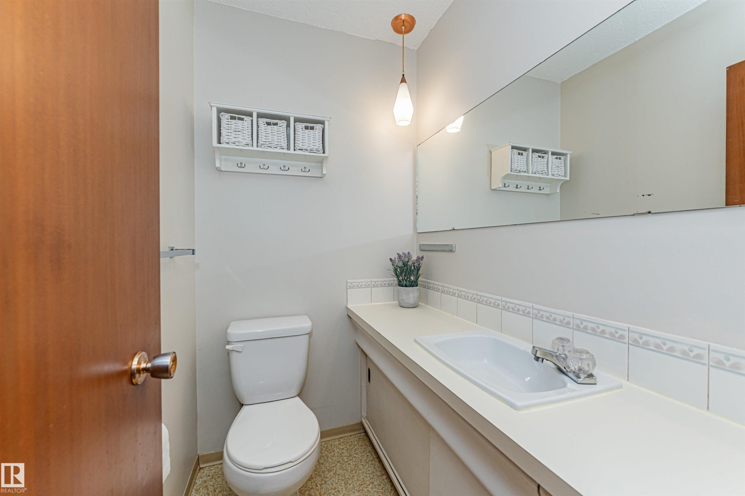 Bathroom featuring an integrated vanity sink with a laminate countertop, a full-width mirror, and a toilet - 11423 50 Avenue, Edmonton, AB - Indoor Photo Showing Bathroom