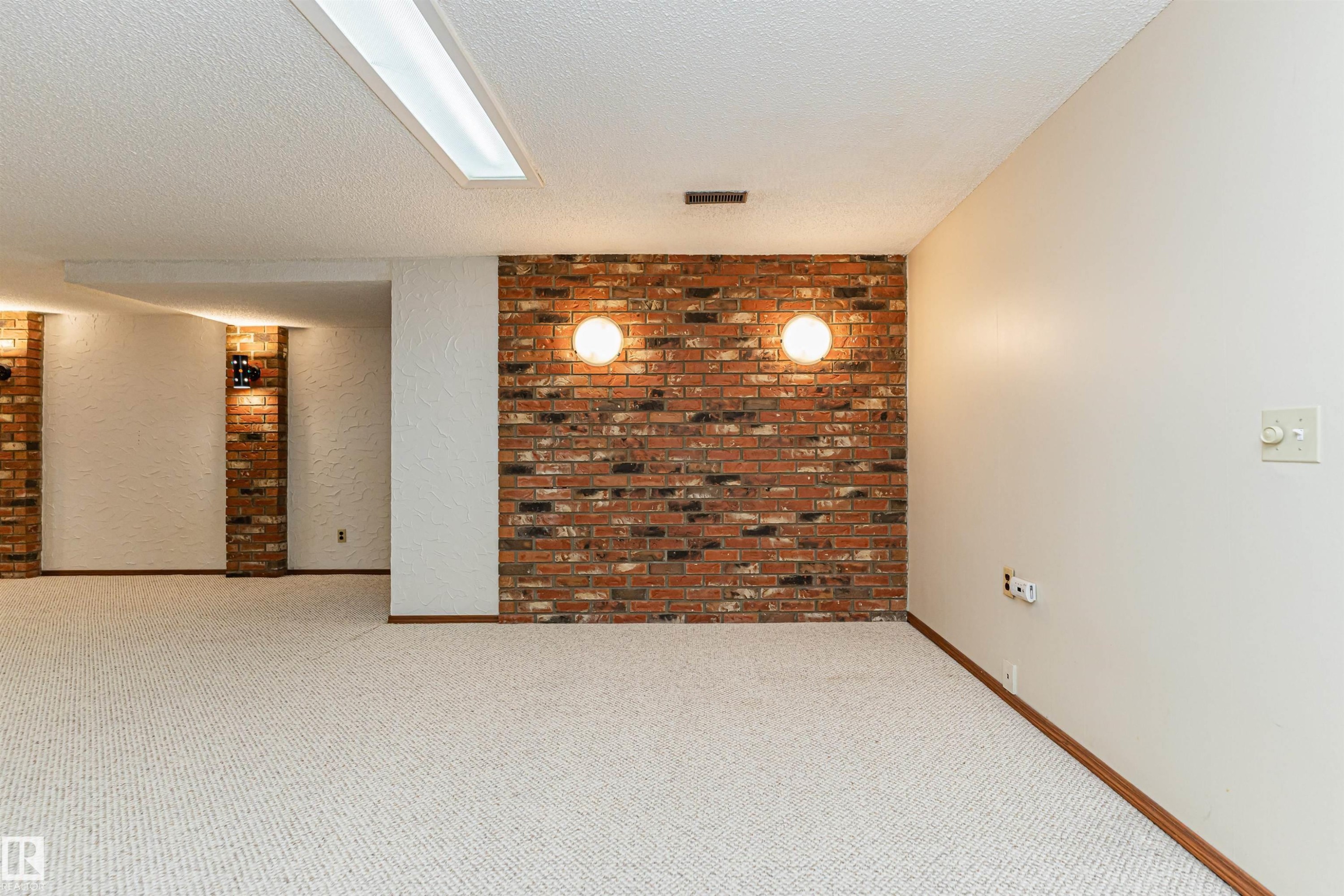 Spacious room featuring light-toned carpeting and exposed brick accent walls with sconce lighting - 11423 50 Avenue, Edmonton, AB - Indoor Photo Showing Other Room