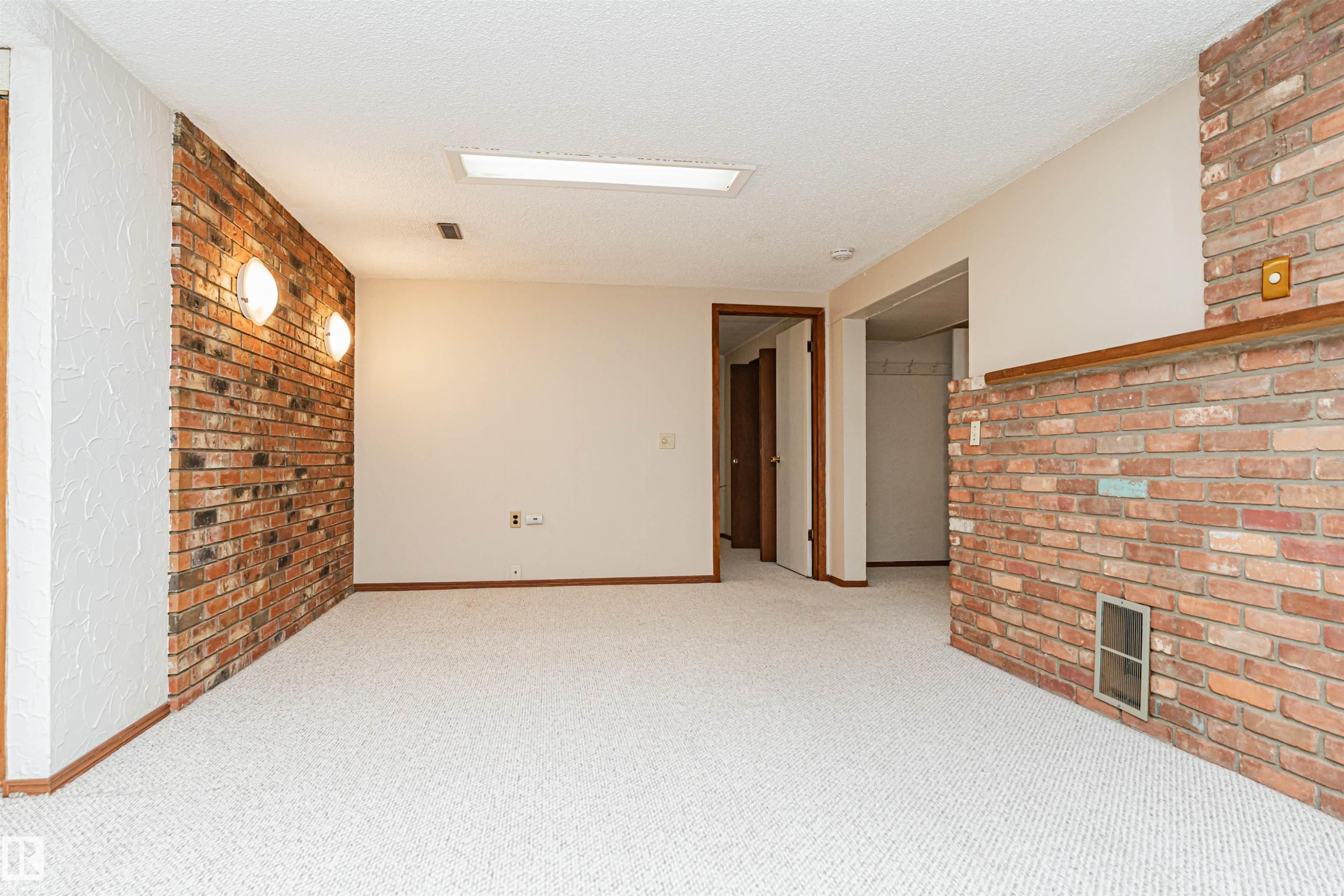 Bright white carpeted space featuring a full brick accent wall with two sconce lights, a recessed light, and a brick half-wall with a wood mantel - 11423 50 Avenue, Edmonton, AB - Indoor Photo Showing Other Room