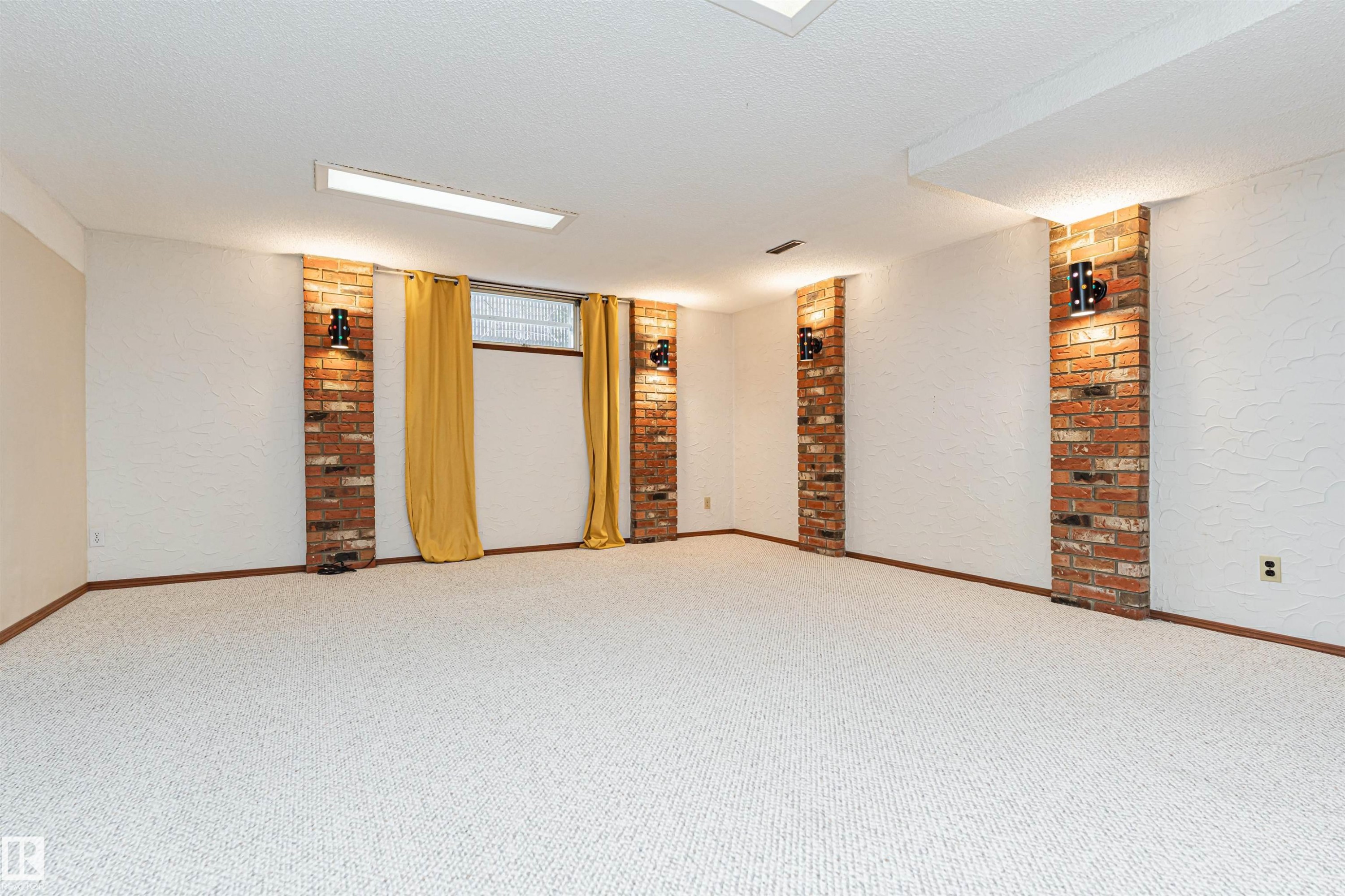 Spacious room featuring light-colored carpeting, white textured walls, and exposed brick columns - 11423 50 Avenue, Edmonton, AB - Indoor Photo Showing Other Room