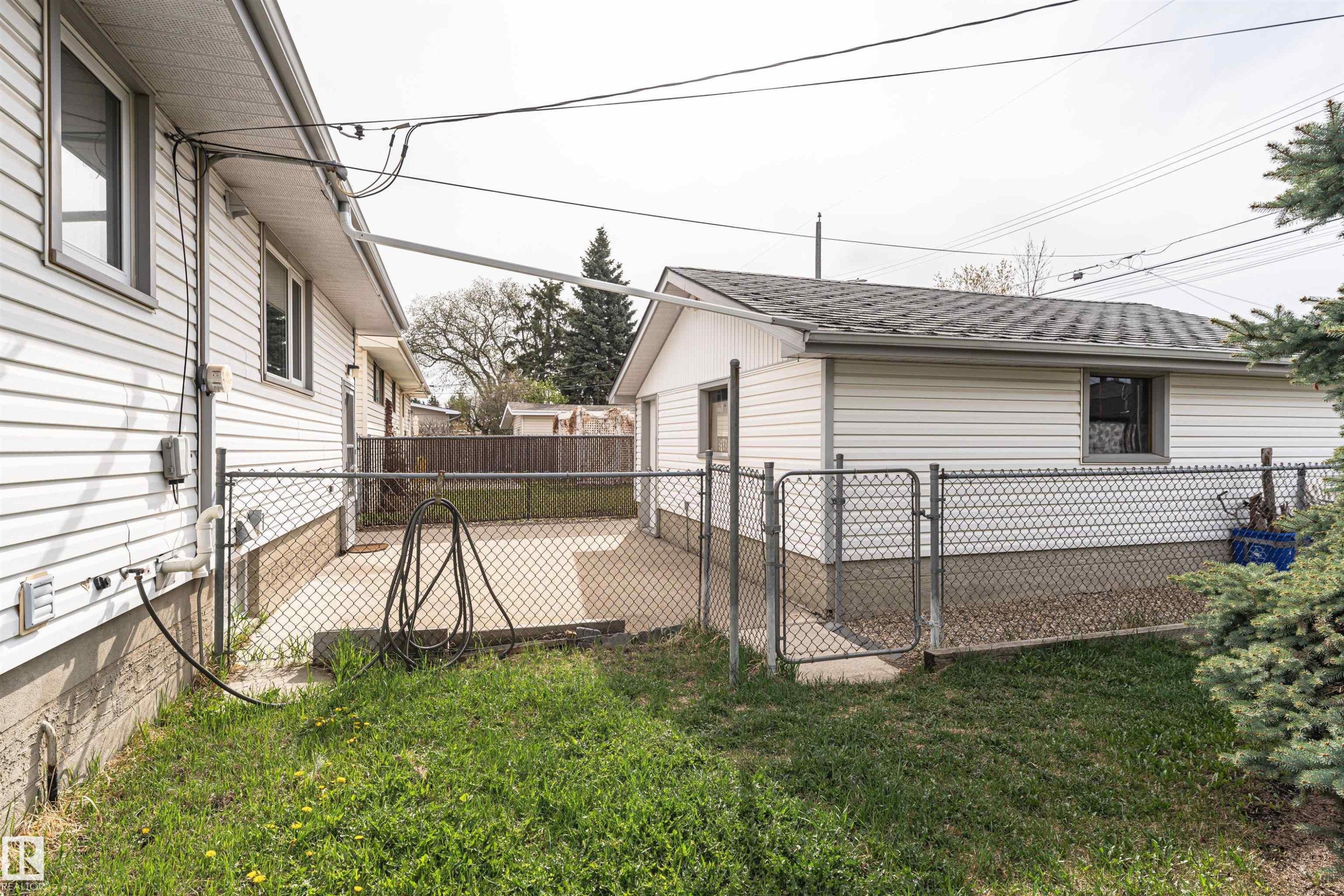 Chain-link fenced yard space featuring a concrete patio, a detached structure with vinyl siding, and a small grassy area - 11423 50 Avenue, Edmonton, AB - Outdoor With Deck Patio Veranda With Exterior