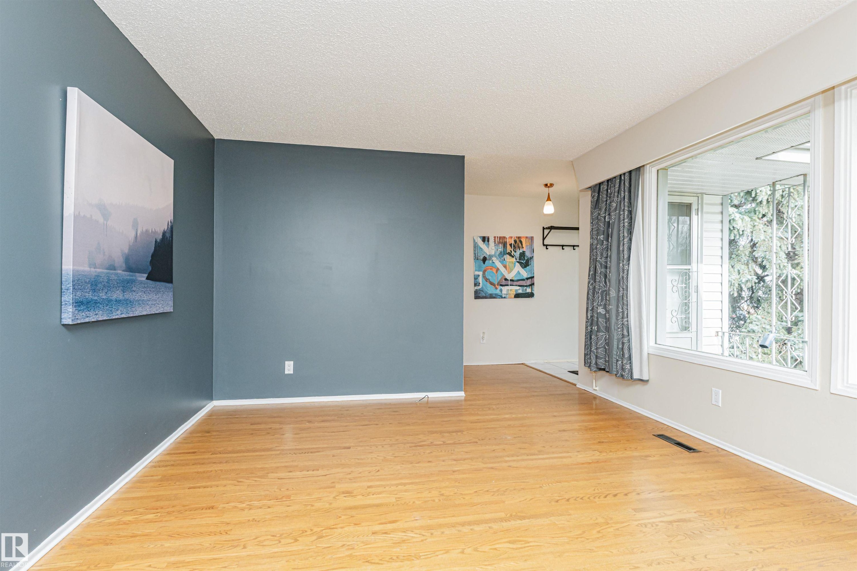 Bright interior space featuring wood-finish flooring, a prominent bay window with white trim, and a high ceiling - 11423 50 Avenue, Edmonton, AB - Indoor Photo Showing Other Room