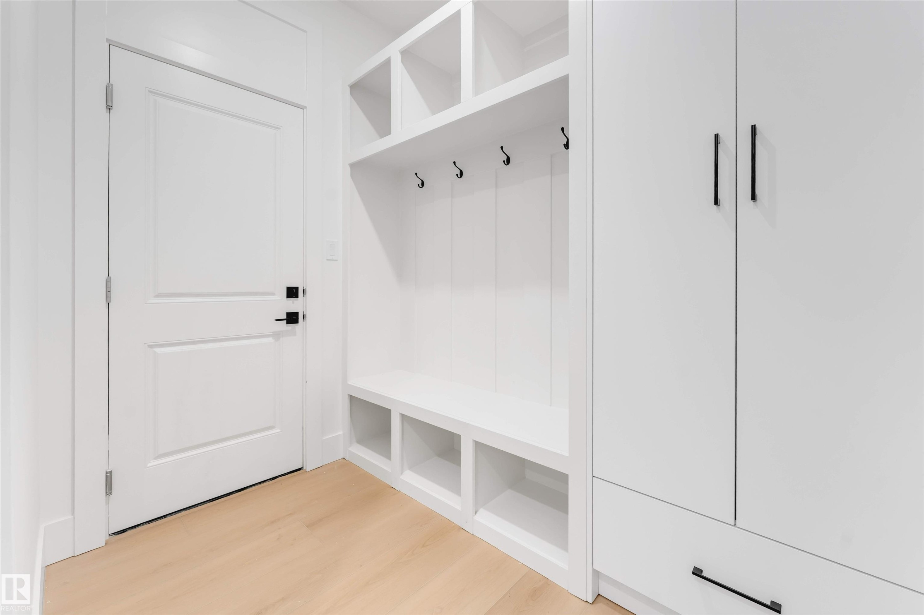 Entryway featuring light hardwood floors, a white paneled door with black hardware, and a built-in storage unit with shelving, hooks, and cabinets - 4004 35 Street, Beaumont, AB - Indoor Photo Showing Other Room