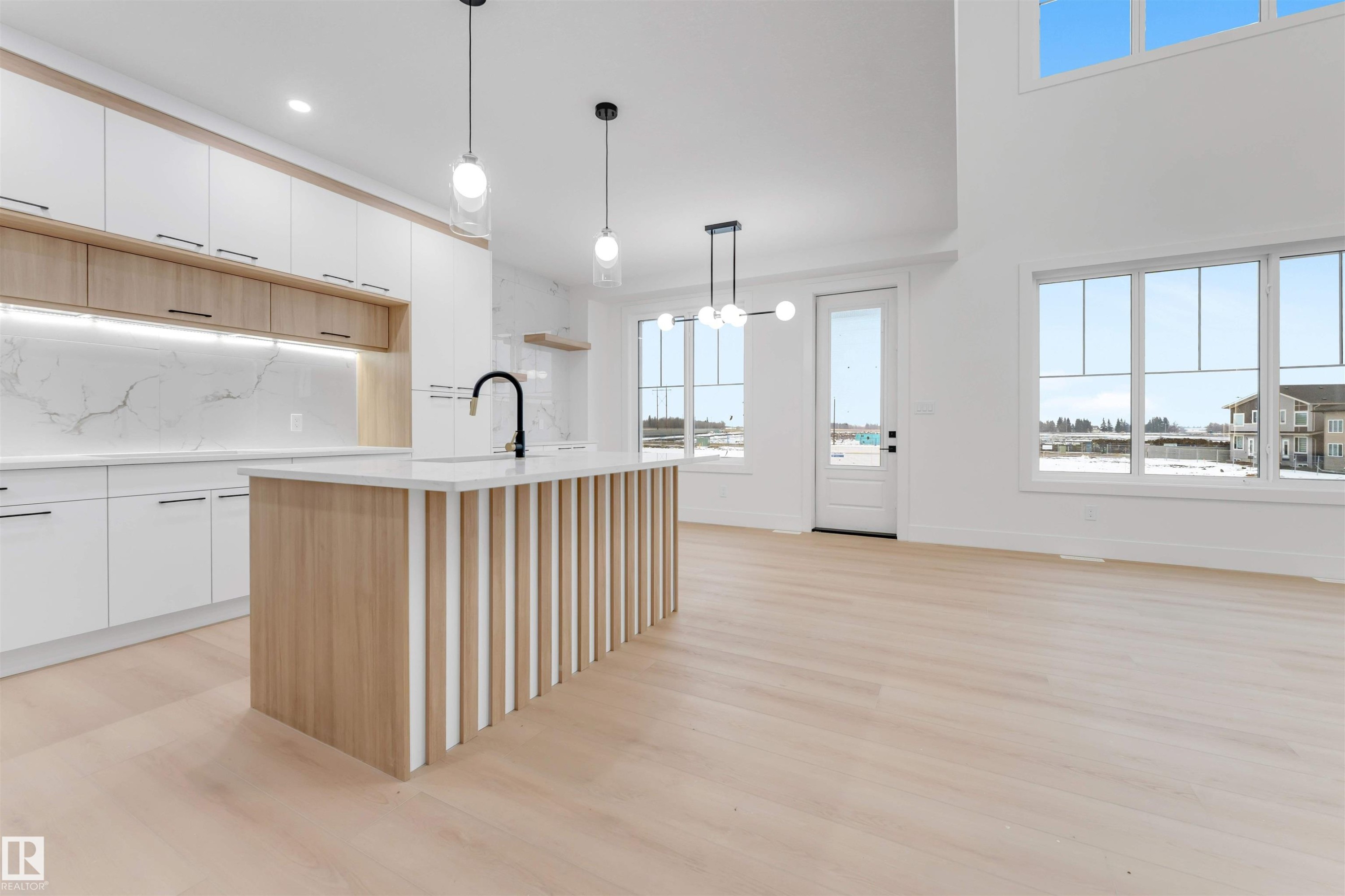 The kitchen features a contemporary island with a light wood base and vertical slat detailing, complemented by white cabinetry, a marble-patterned backsplash, and a modern black faucet - 4004 35 Street, Beaumont, AB - Indoor Photo Showing Kitchen With Upgraded Kitchen