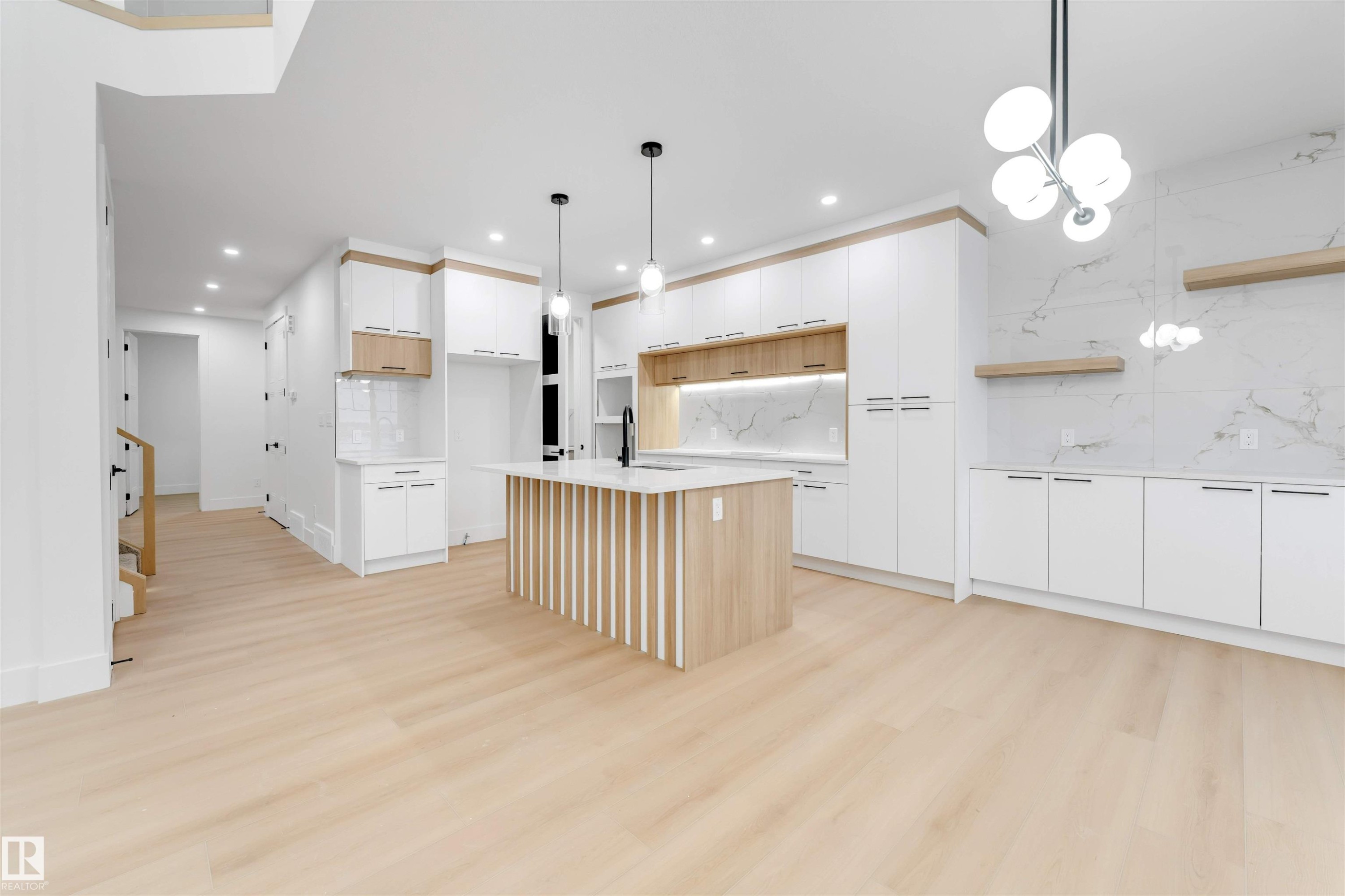 The spacious open-concept living area features light wood flooring, a kitchen island with a light wood base and white countertop, and white cabinetry with light wood accents - 4004 35 Street, Beaumont, AB - Indoor Photo Showing Kitchen