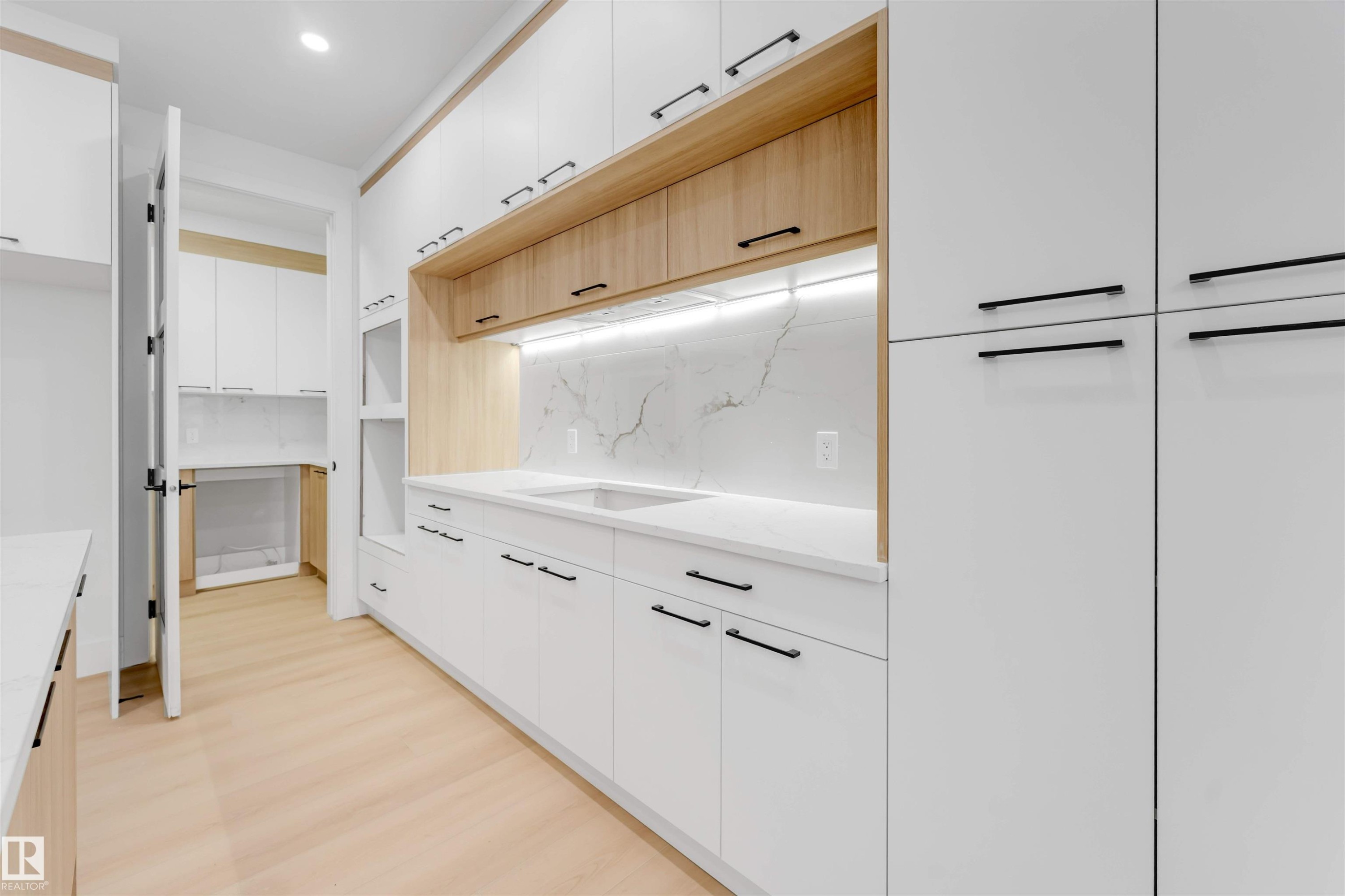 Kitchenette featuring white cabinetry with black hardware, wood accents, a sink, and a white countertop with a matching backsplash - 4004 35 Street, Beaumont, AB - Indoor Photo Showing Other Room