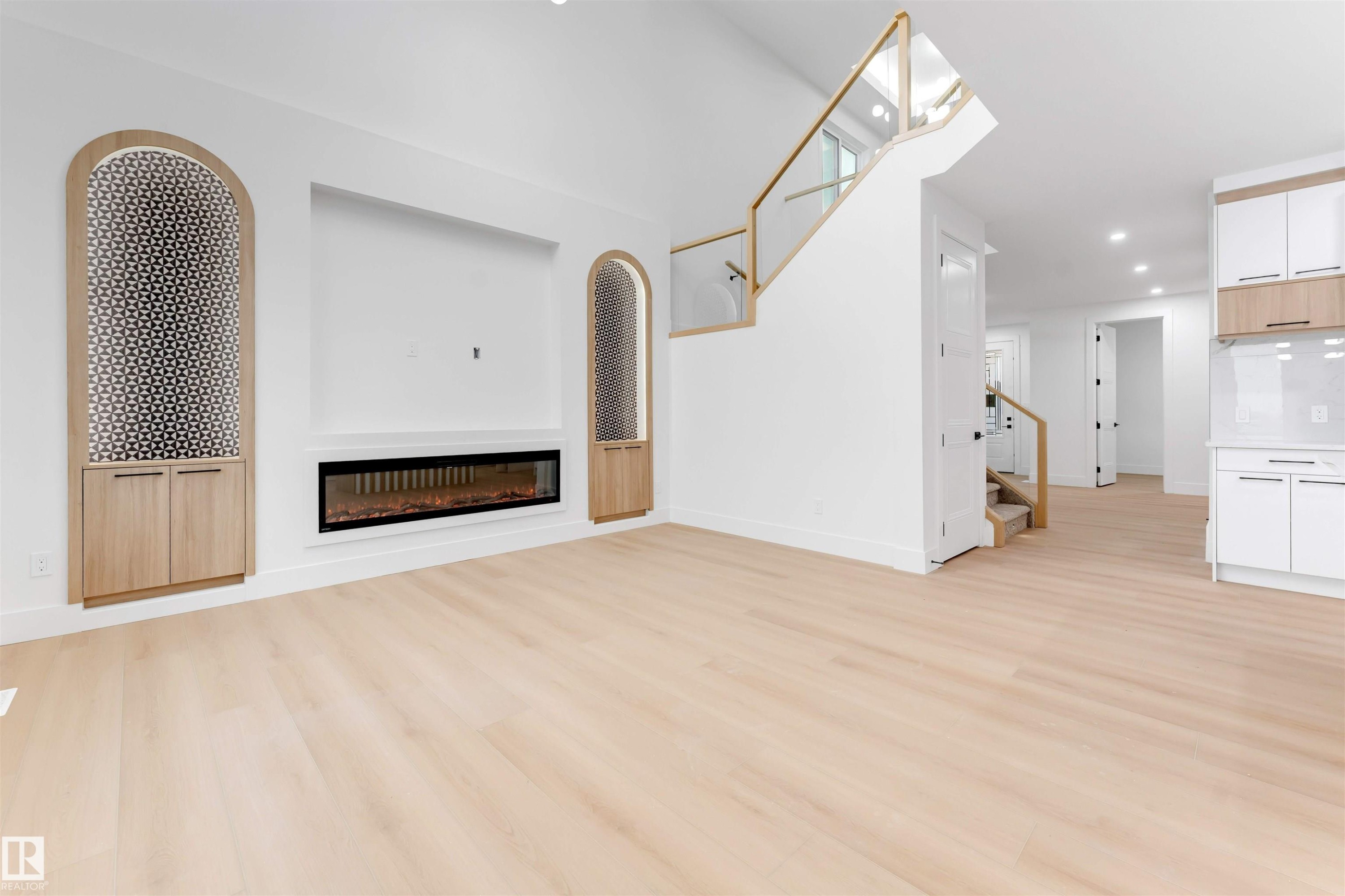 Open concept living space featuring light hardwood flooring, a modern linear fireplace, built-in cabinetry with decorative arched details, and a staircase with glass railings and wood accents - 4004 35 Street, Beaumont, AB - Indoor With Fireplace