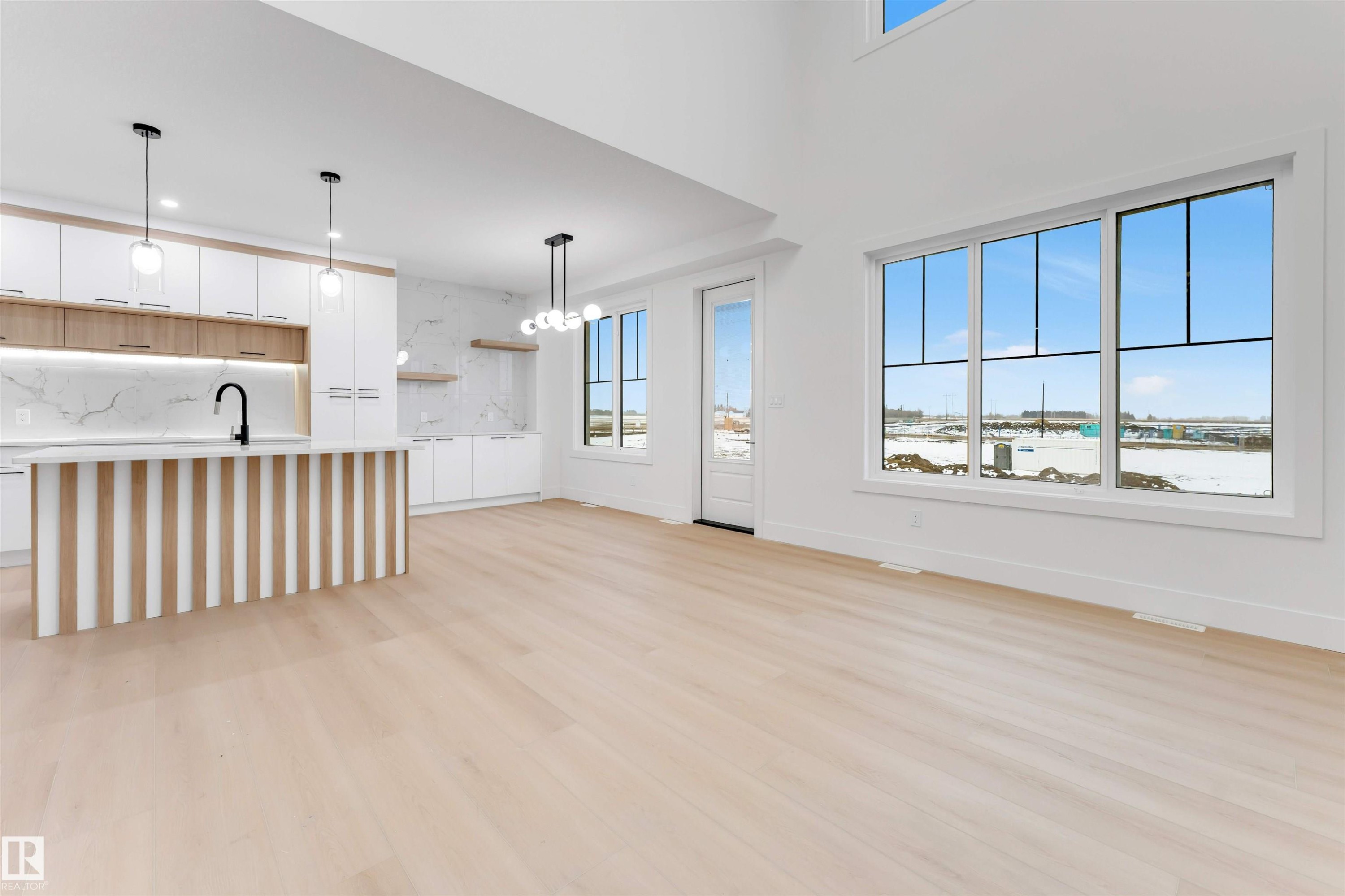 The property features an open-concept layout with light-toned flooring, large windows, and high ceilings - 4004 35 Street, Beaumont, AB - Indoor Photo Showing Kitchen