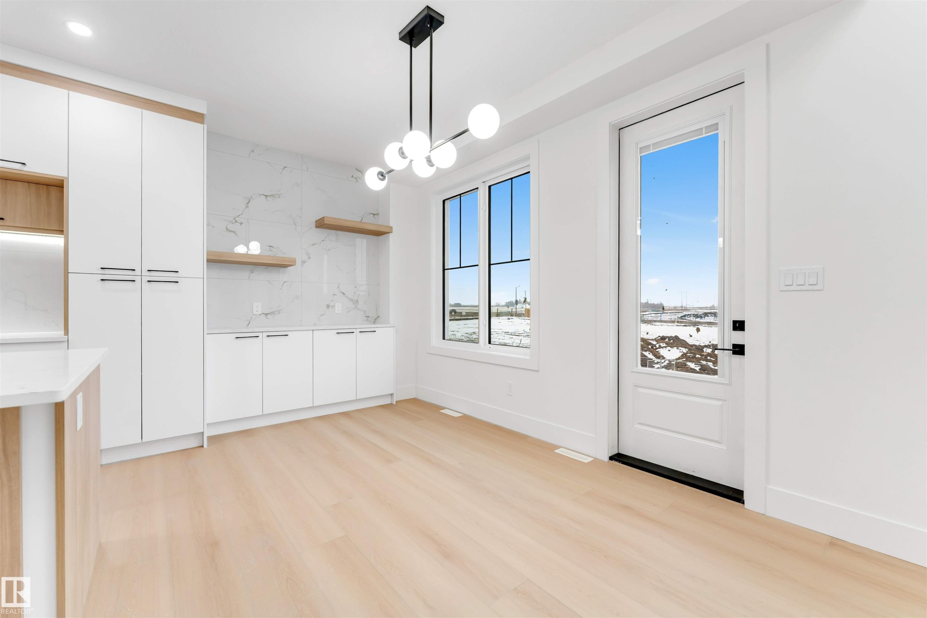 The property features light wood flooring, a modern chandelier, and a white door with a window providing outdoor views - 4004 35 Street, Beaumont, AB - Indoor Photo Showing Other Room