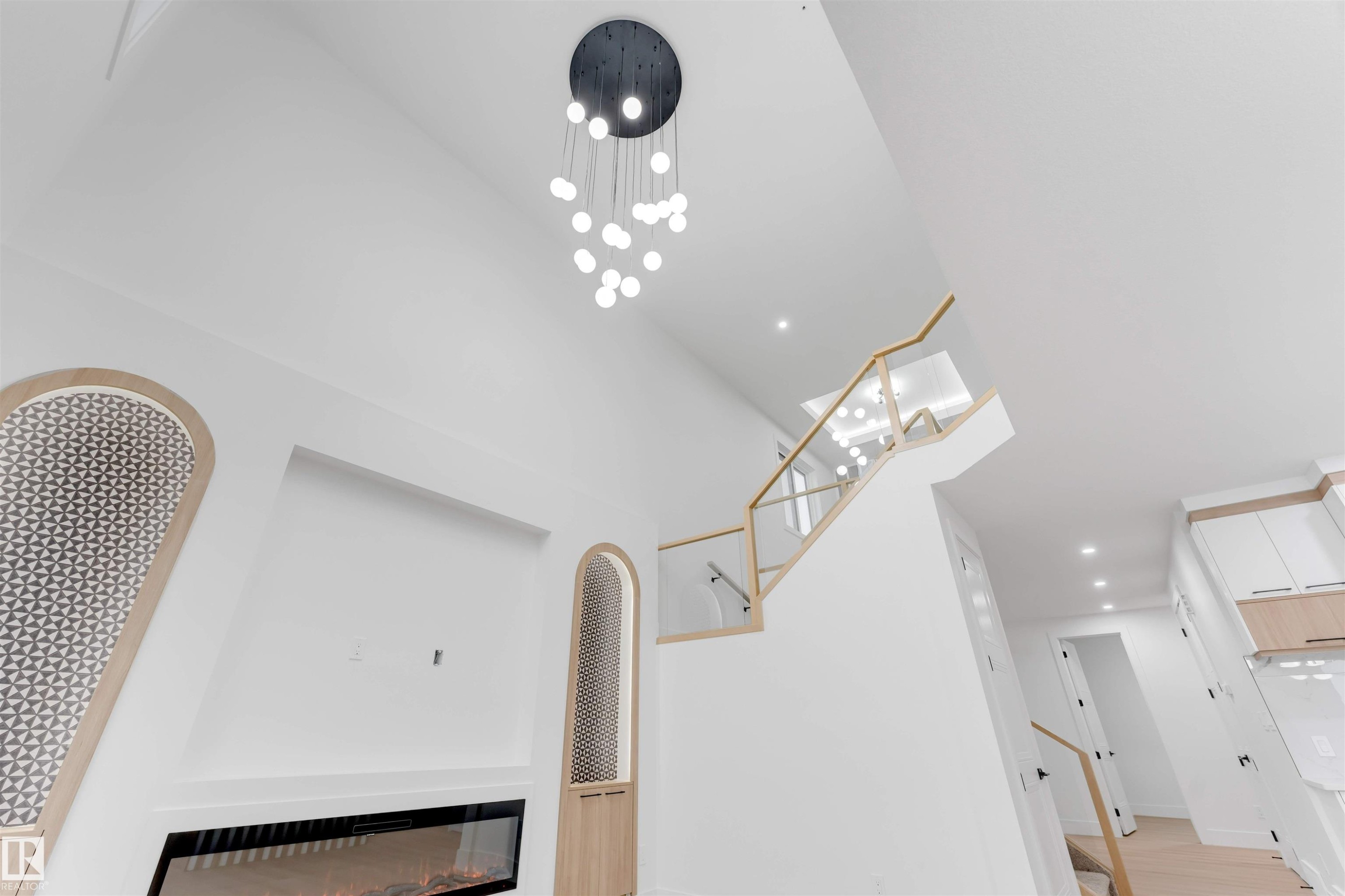 This interior features a high ceiling with a modern chandelier, a contemporary fireplace, and a staircase with a glass railing and light wood handrails - 4004 35 Street, Beaumont, AB - Indoor Photo Showing Other Room