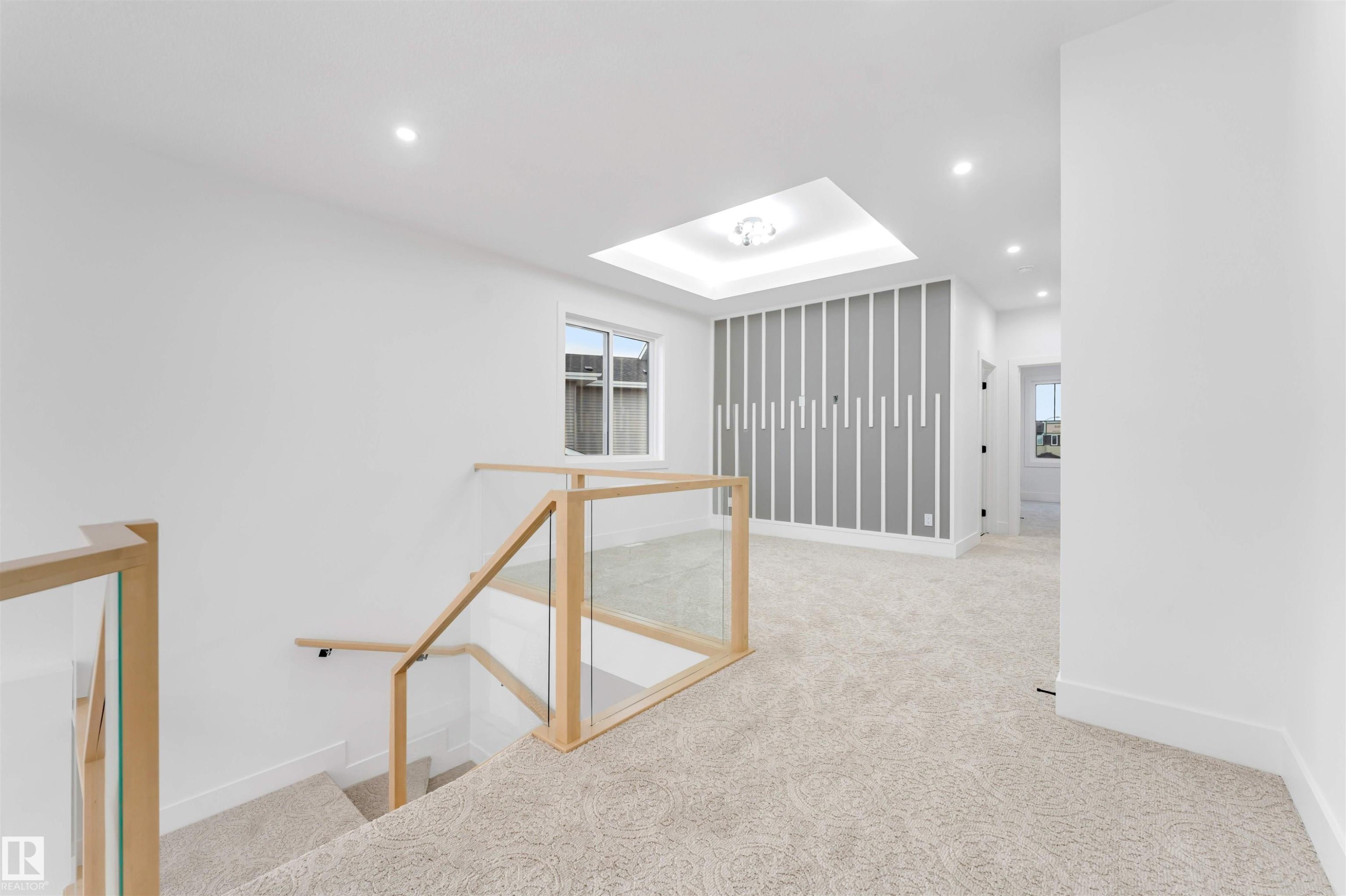 This property features a stairwell with light wood and glass railings, leading to a carpeted landing - 4004 35 Street, Beaumont, AB - Indoor Photo Showing Other Room