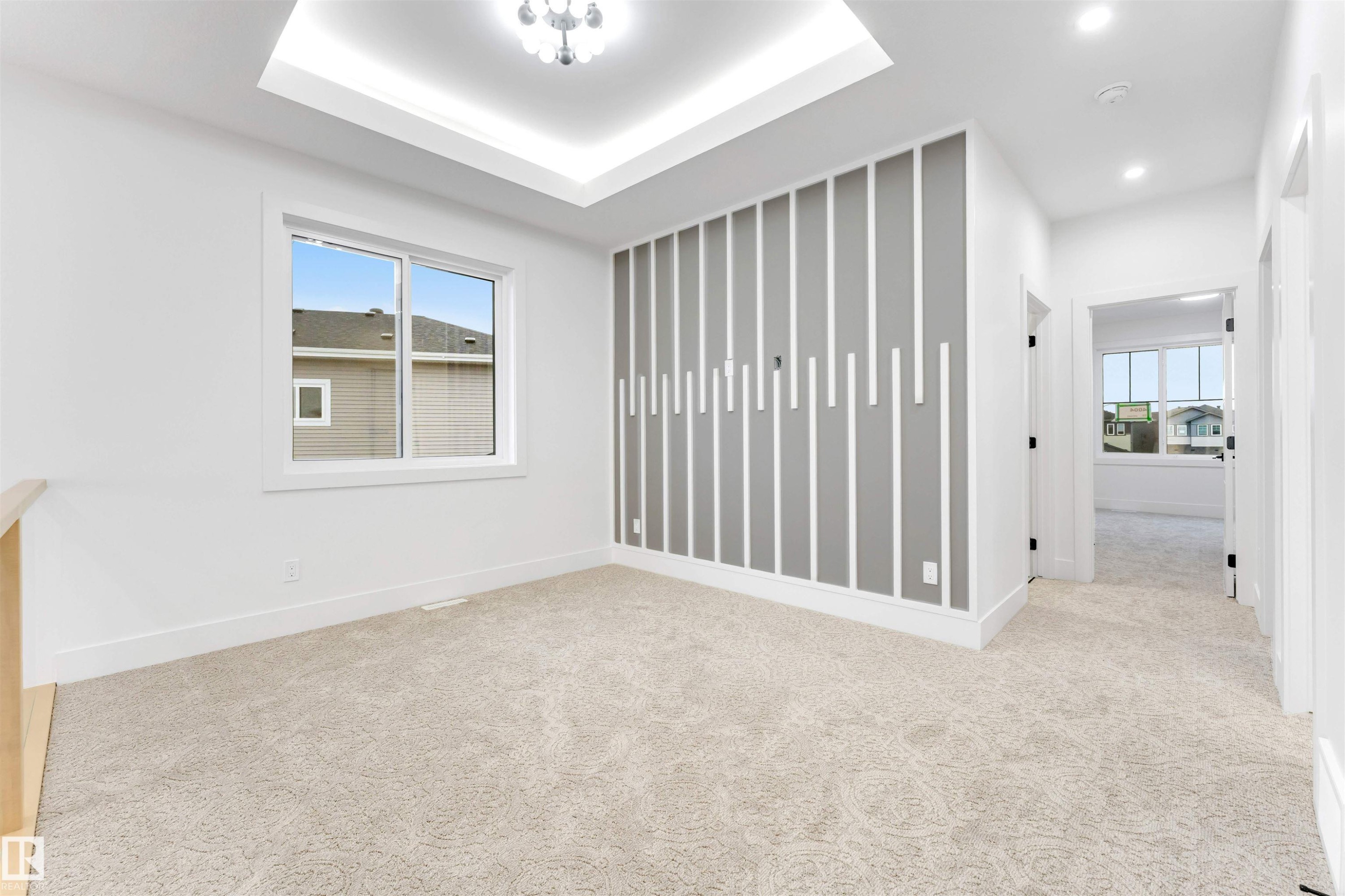This bright room features a decorative accent wall, a window providing natural light, and plush carpet flooring, complemented by a tray ceiling with an overhead light fixture - 4004 35 Street, Beaumont, AB - Indoor Photo Showing Other Room