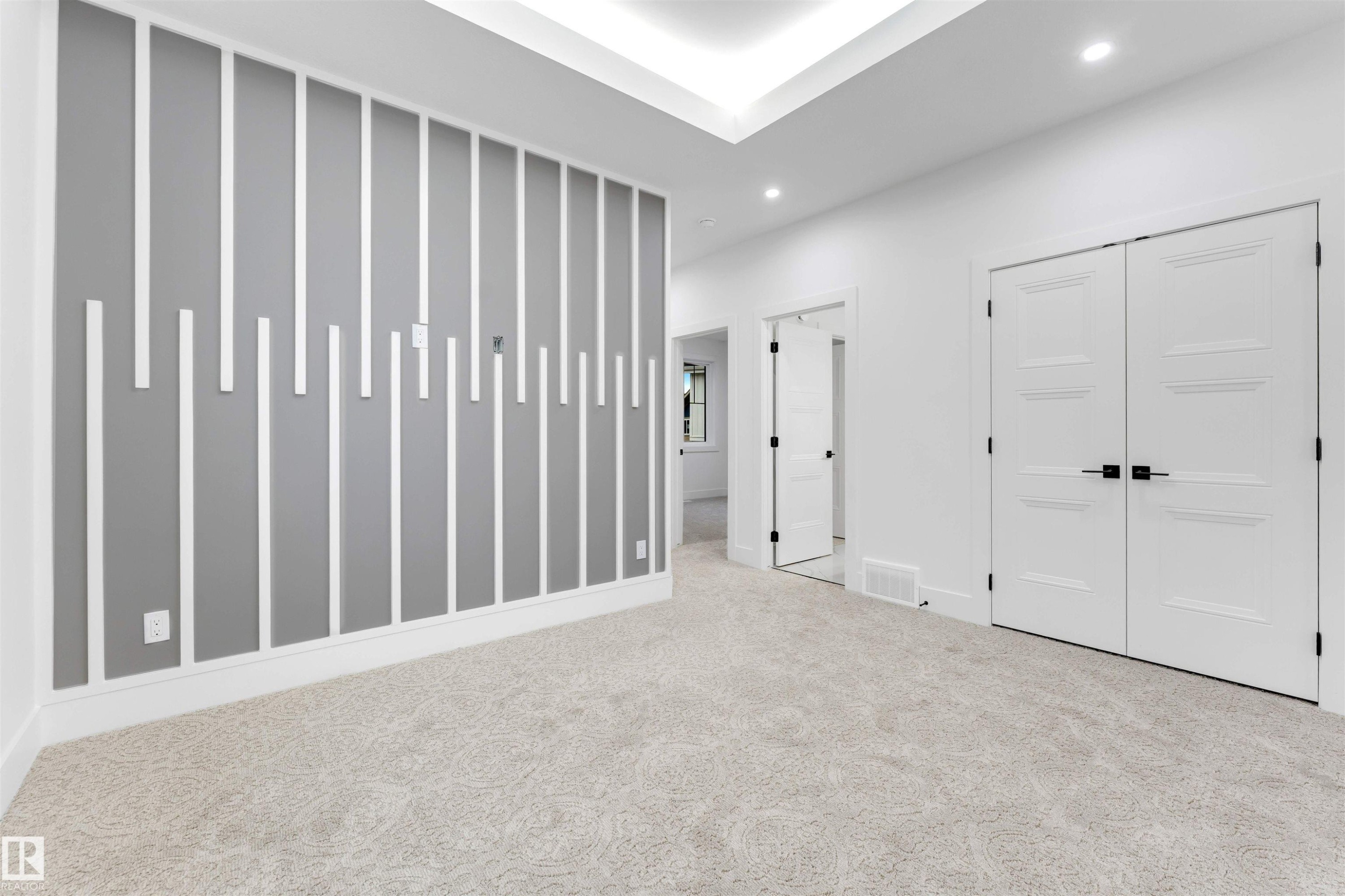 Spacious room featuring light-colored carpet, a decorative accent wall with vertical white trim, and a tray ceiling with recessed lighting - 4004 35 Street, Beaumont, AB - Indoor Photo Showing Other Room
