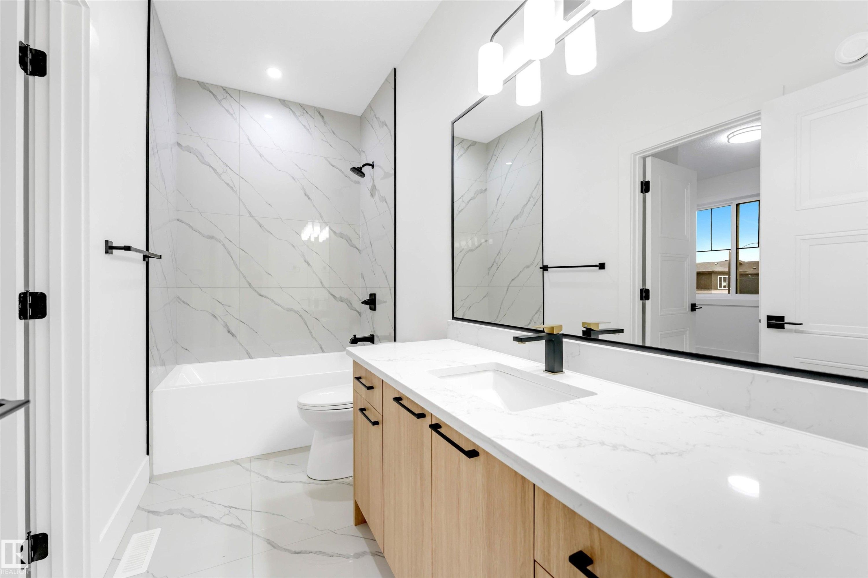 The bathroom features a modern vanity with a white countertop and a rectangular undermount sink, a large mirror with integrated lighting, and a bathtub with white and grey marbled tile surround - 4004 35 Street, Beaumont, AB - Indoor Photo Showing Bathroom