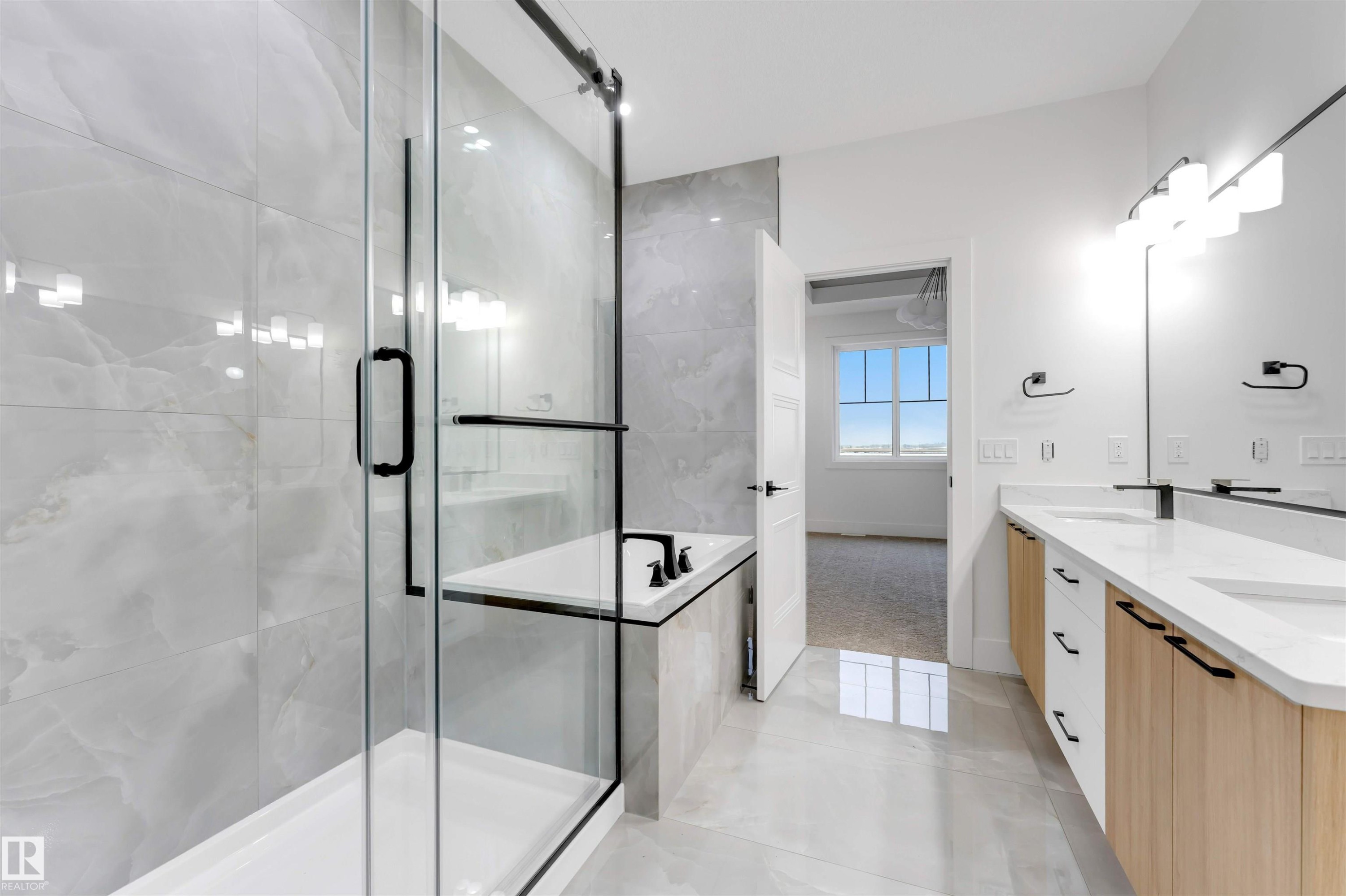 A spacious bathroom featuring a glass-enclosed shower with black trim, a standalone bathtub, and a double vanity with light wood cabinetry and white countertops - 4004 35 Street, Beaumont, AB - Indoor Photo Showing Bathroom
