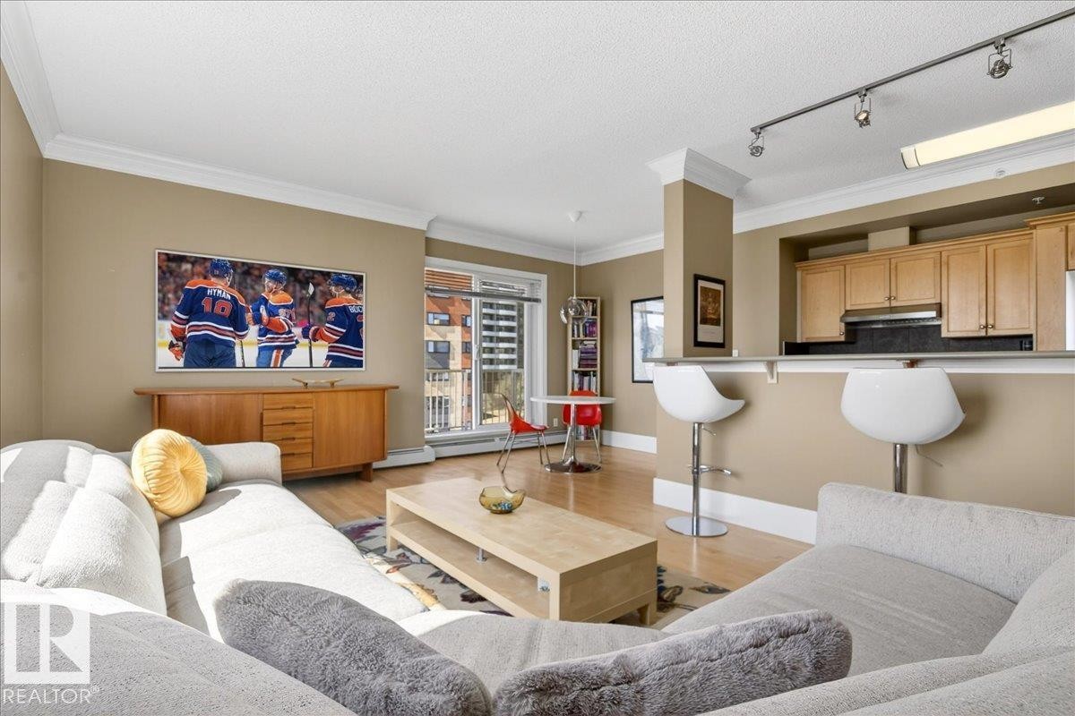 Open-concept living space featuring wood-finish flooring, crown molding, and a kitchen bar with track lighting - 701 9707 105 Street, Edmonton, AB - Indoor Photo Showing Living Room