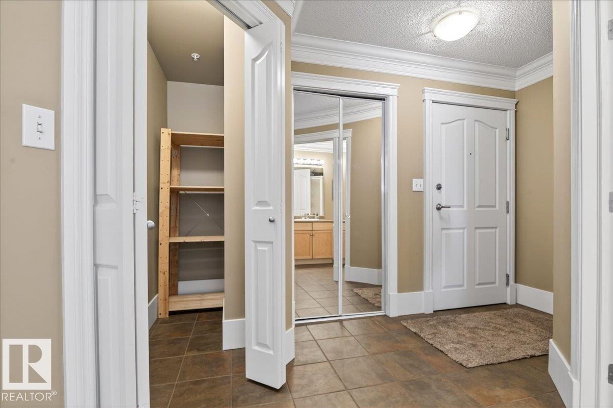 Tiled entry foyer featuring a white paneled door, crown molding, baseboards, and a flush mount ceiling light - 701 9707 105 Street, Edmonton, AB - Indoor Photo Showing Other Room