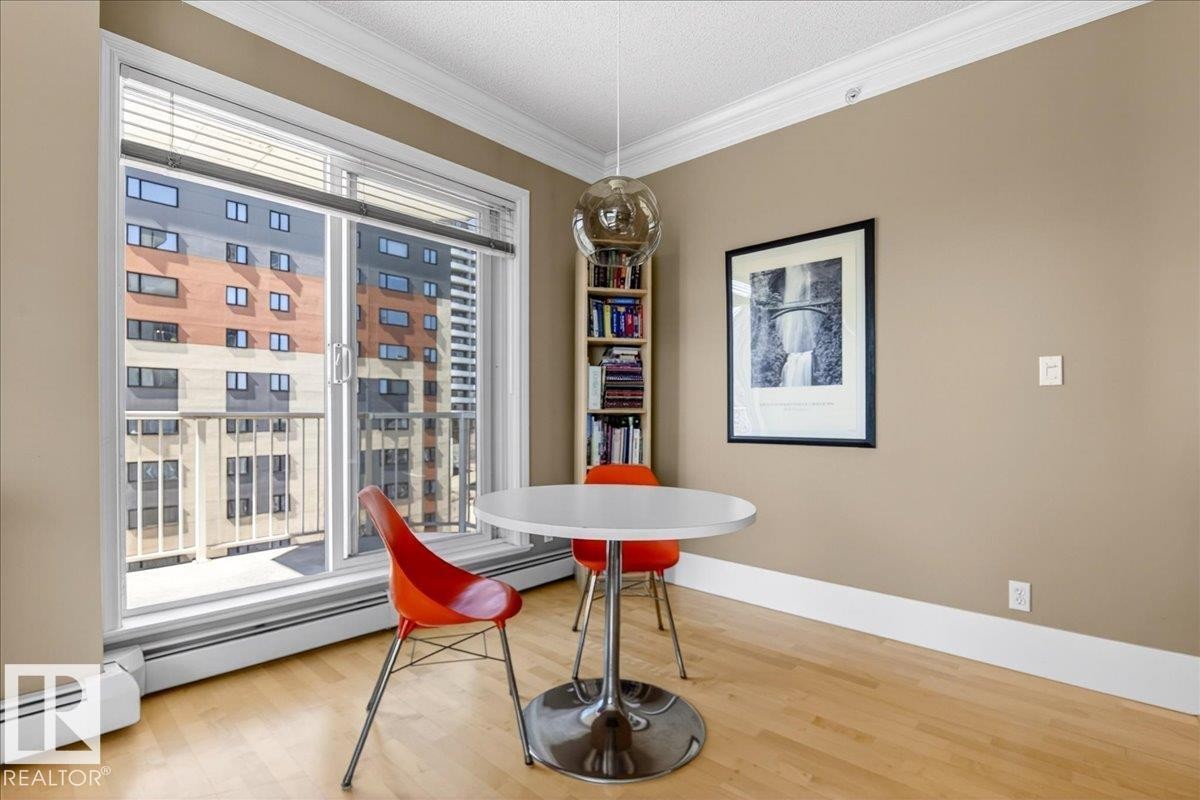 Sliding glass doors leading to a balcony, light wood-finish flooring, built-in shelving, crown molding, and neutral wall tones - 701 9707 105 Street, Edmonton, AB - Indoor