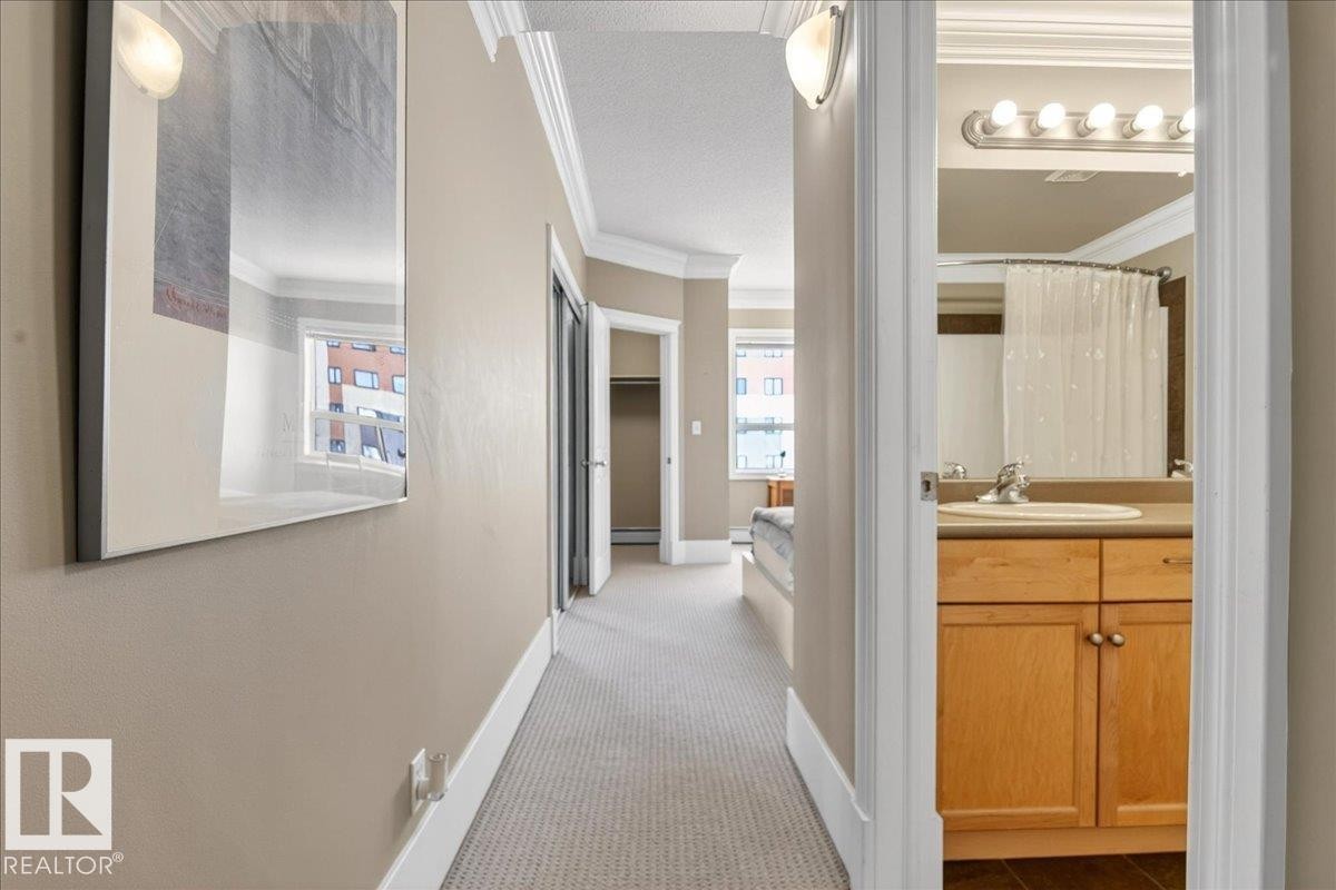 Hallway featuring carpet flooring, crown molding, and a wall sconce - 701 9707 105 Street, Edmonton, AB - Indoor Photo Showing Other Room