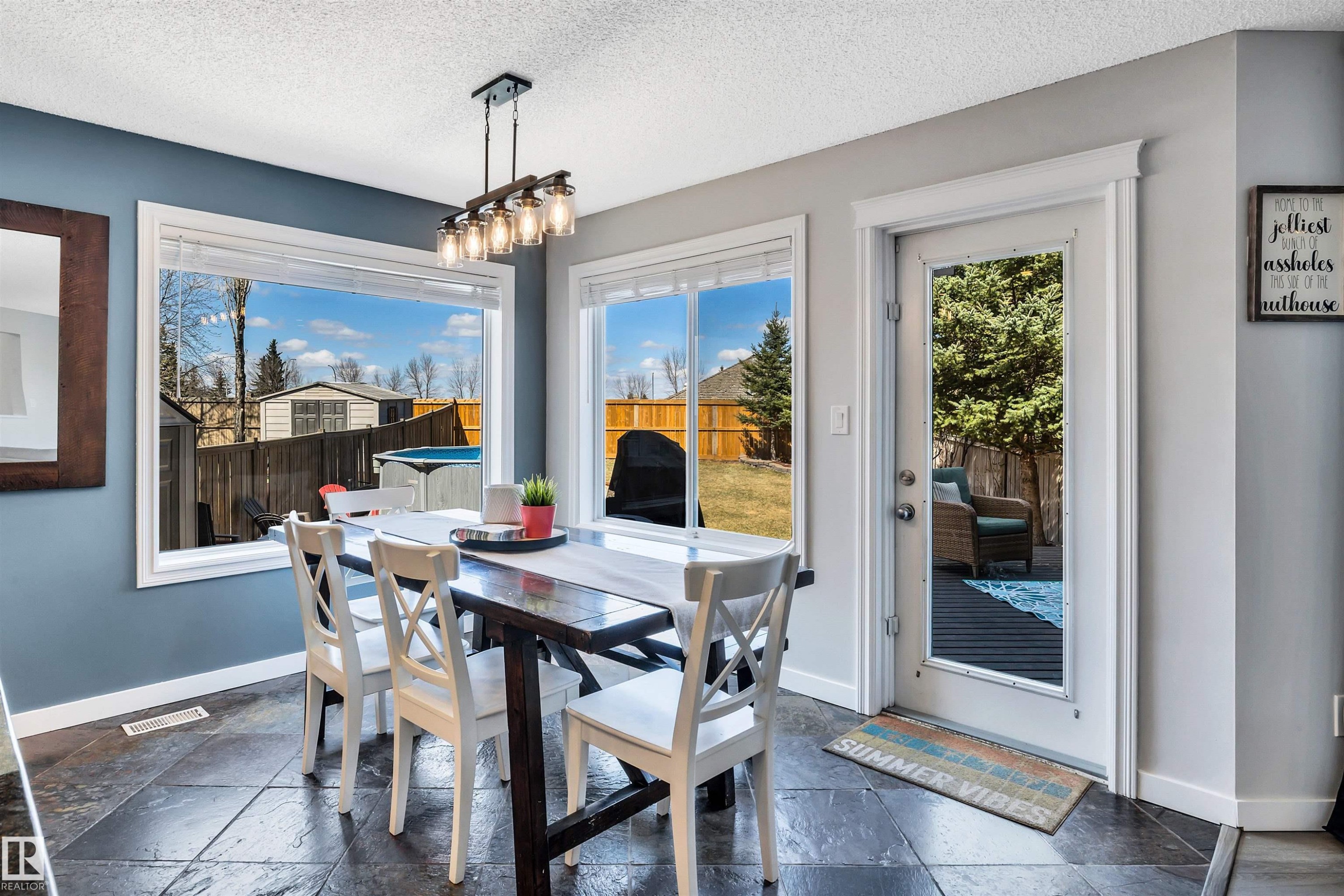 Dining area featuring large windows, a full-lite exterior door, dark square tile flooring, and an industrial-style chandelier - 96 Bonin Crescent, Beaumont, AB - Indoor Photo Showing Dining Room