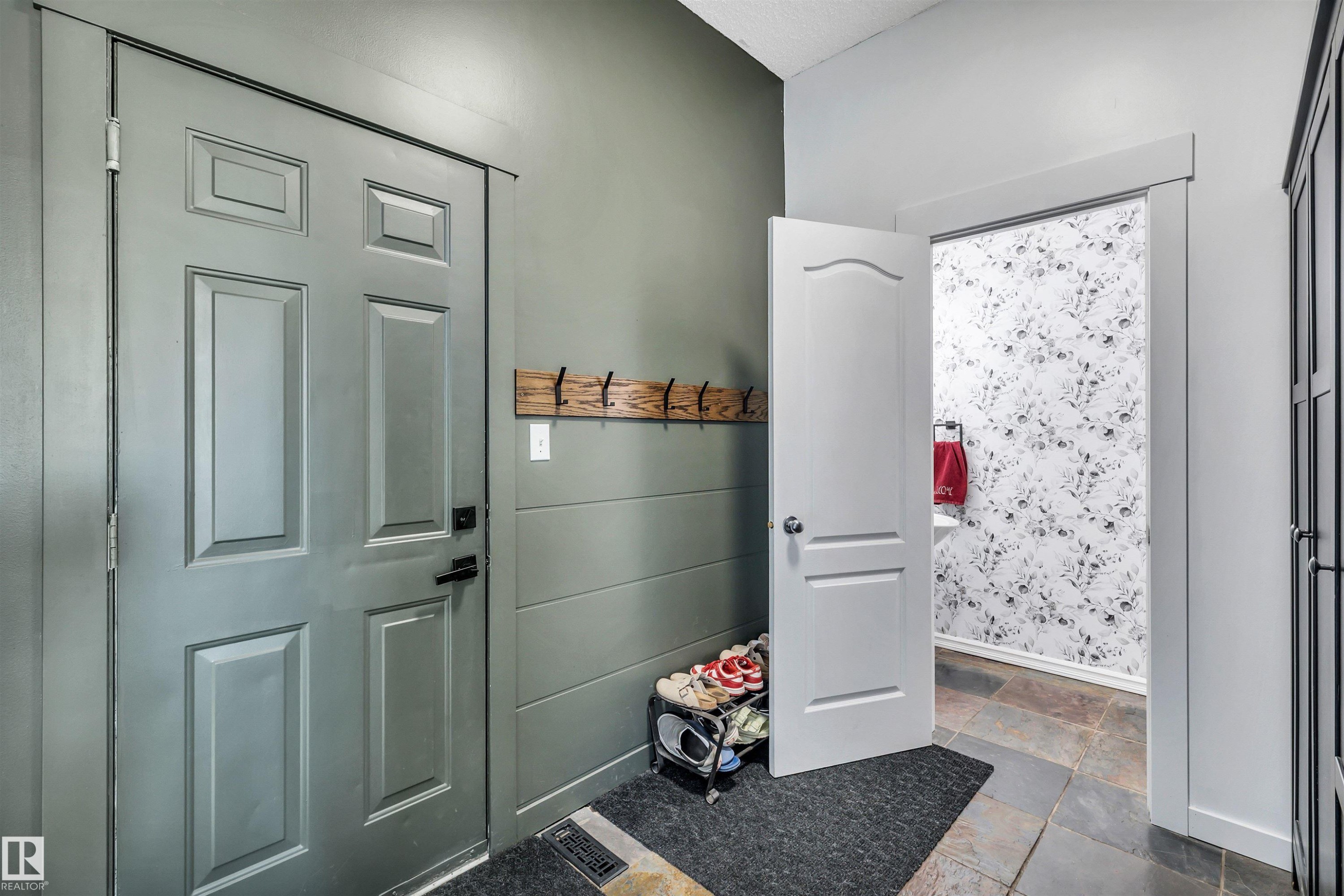 Entryway featuring a paneled door with black hardware, shiplap-style wall detailing, a wooden coat rack, and slate-finish floor tiles - 96 Bonin Crescent, Beaumont, AB - Indoor Photo Showing Other Room