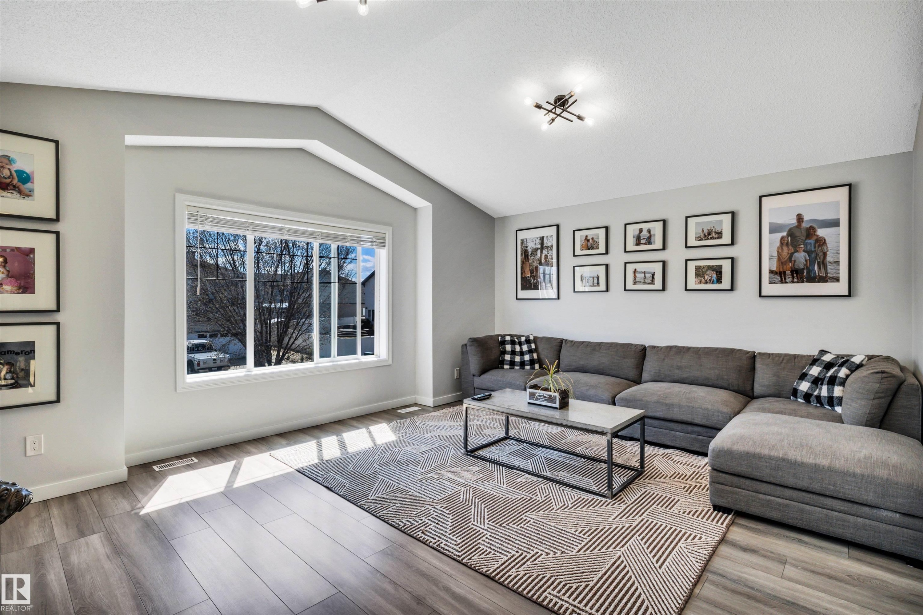 Spacious living area featuring vaulted ceilings, wood-finish flooring, a large multi-pane window, and recessed lighting - 96 Bonin Crescent, Beaumont, AB - Indoor Photo Showing Living Room