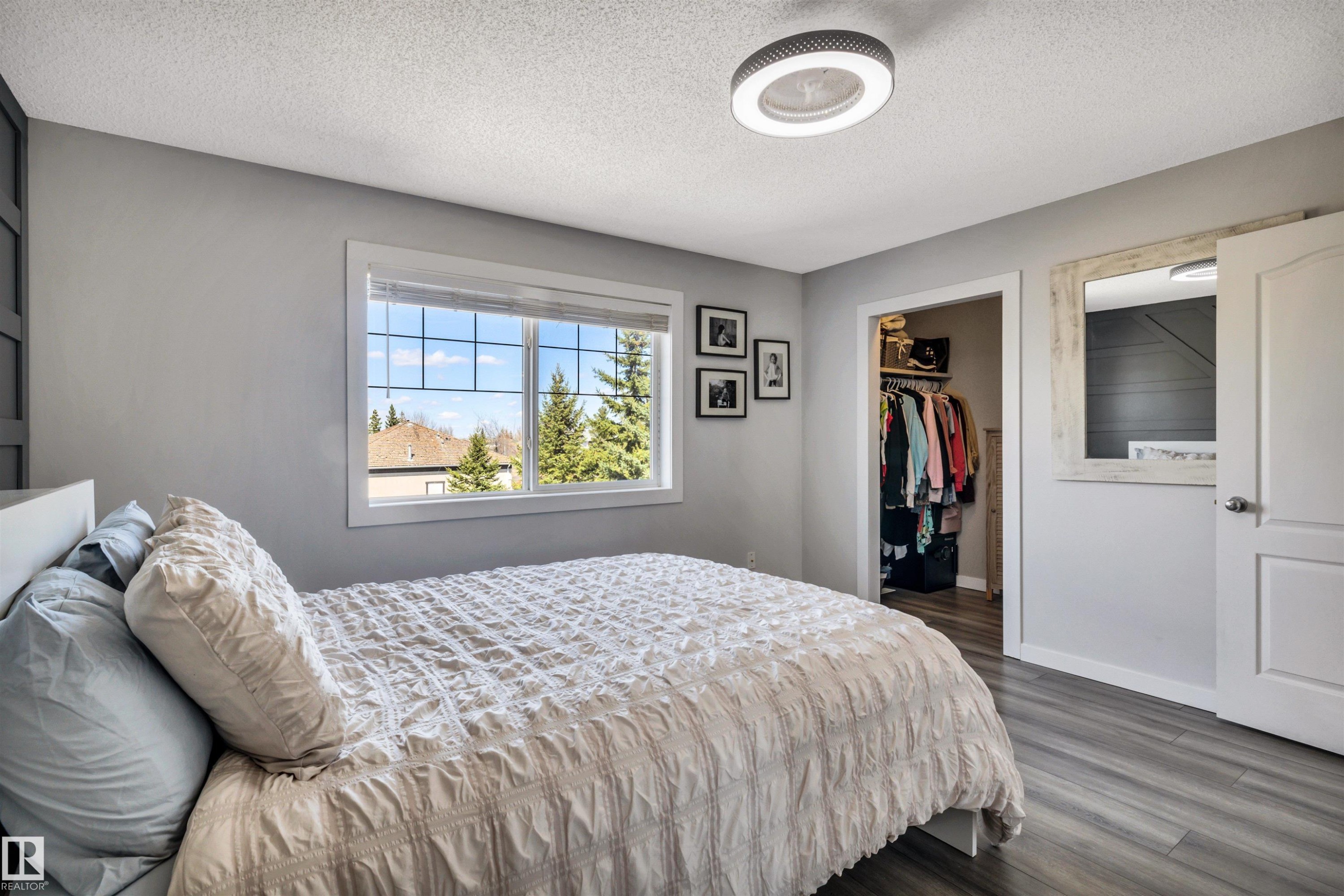 Spacious room featuring wood-finish flooring, a contemporary ceiling light fixture, a large window, and an open closet with built-in shelving - 96 Bonin Crescent, Beaumont, AB - Indoor Photo Showing Bedroom