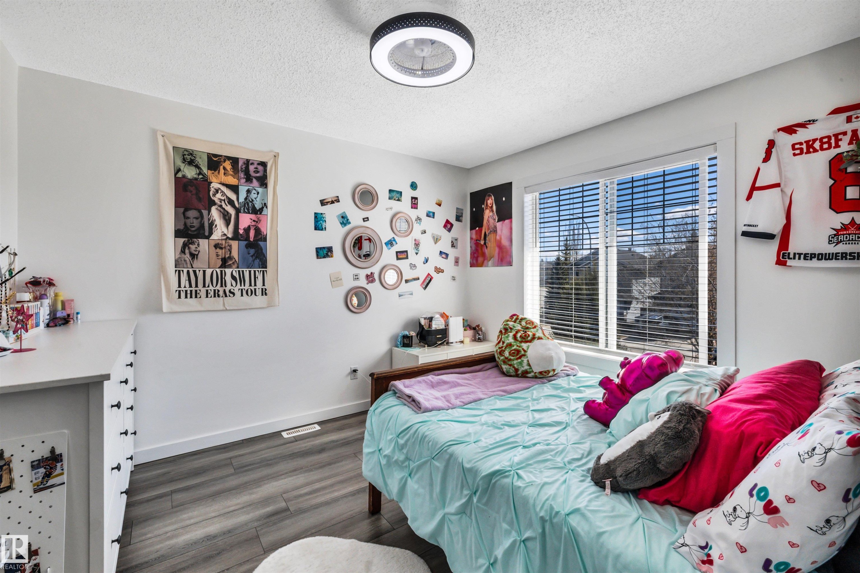 Bedroom featuring a large window with horizontal blinds, wood-finish flooring, and a ceiling-mounted light fixture - 96 Bonin Crescent, Beaumont, AB - Indoor Photo Showing Bedroom