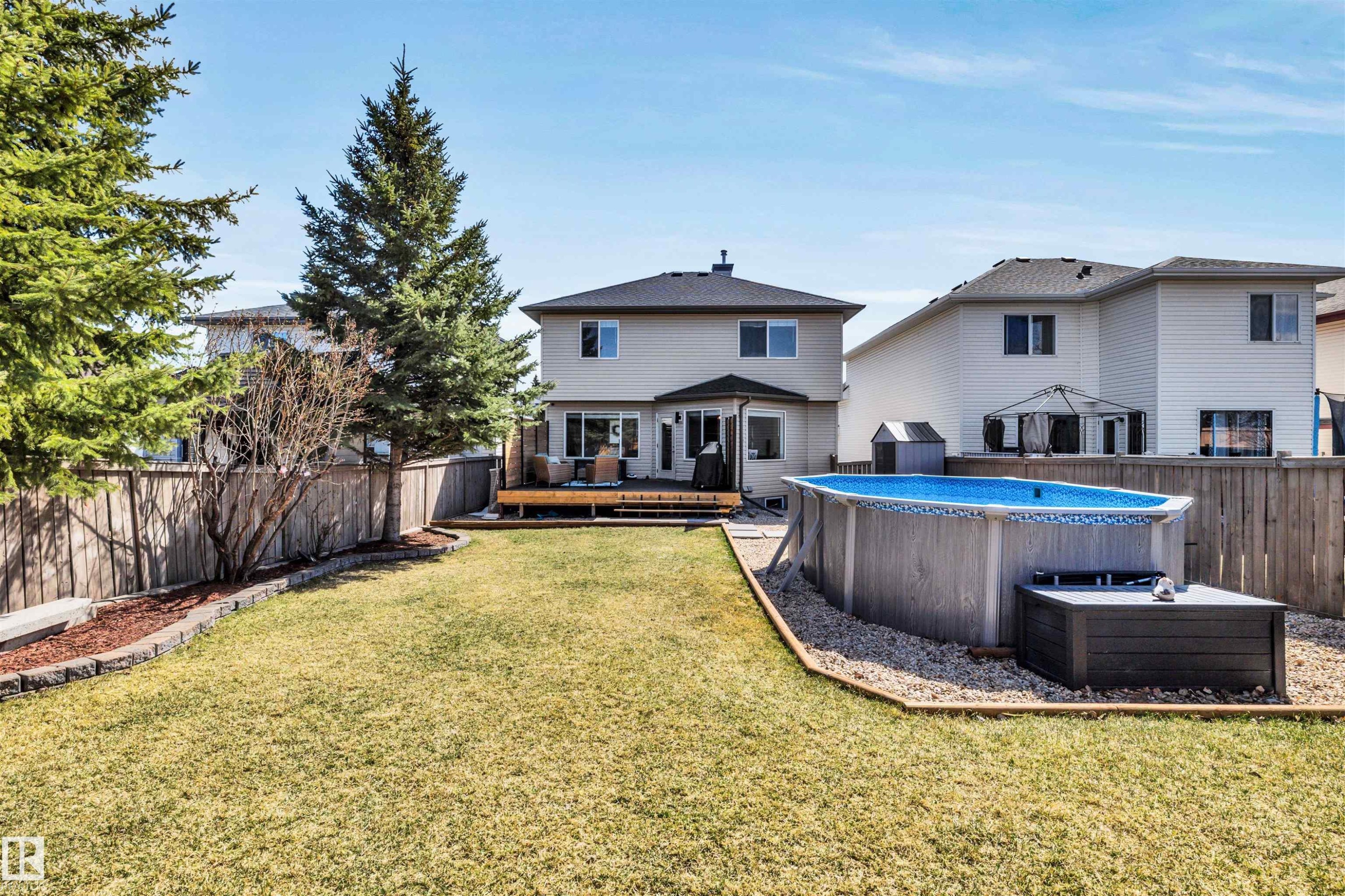 Expansive backyard featuring a manicured lawn, a raised wooden deck, and an above-ground pool with surrounding gravel - 96 Bonin Crescent, Beaumont, AB - Outdoor With Above Ground Pool With Backyard With Exterior