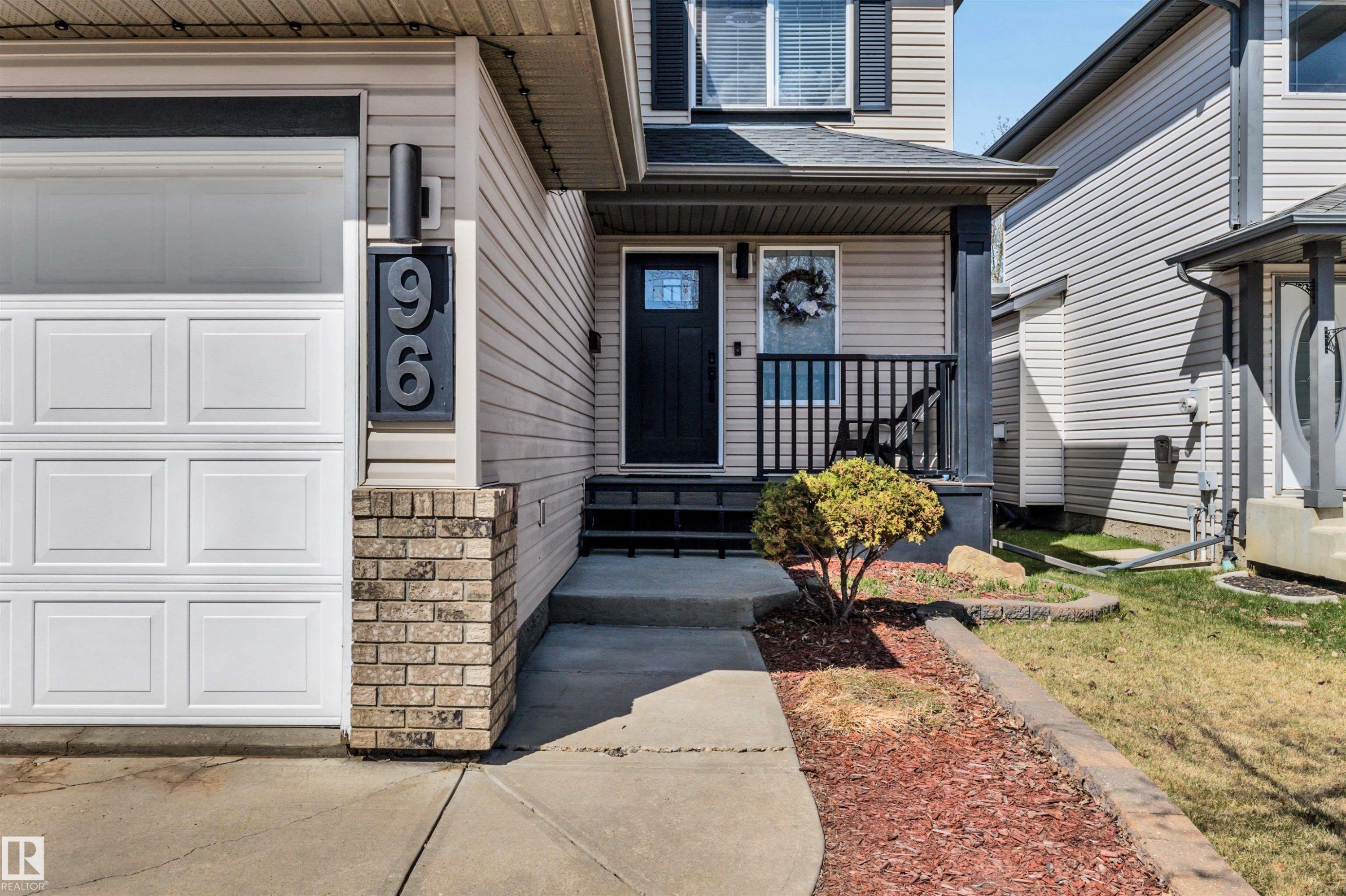 Exterior featuring light-colored siding, a white panel garage door, and a black front door with a glass insert - 96 Bonin Crescent, Beaumont, AB - Outdoor With Facade
