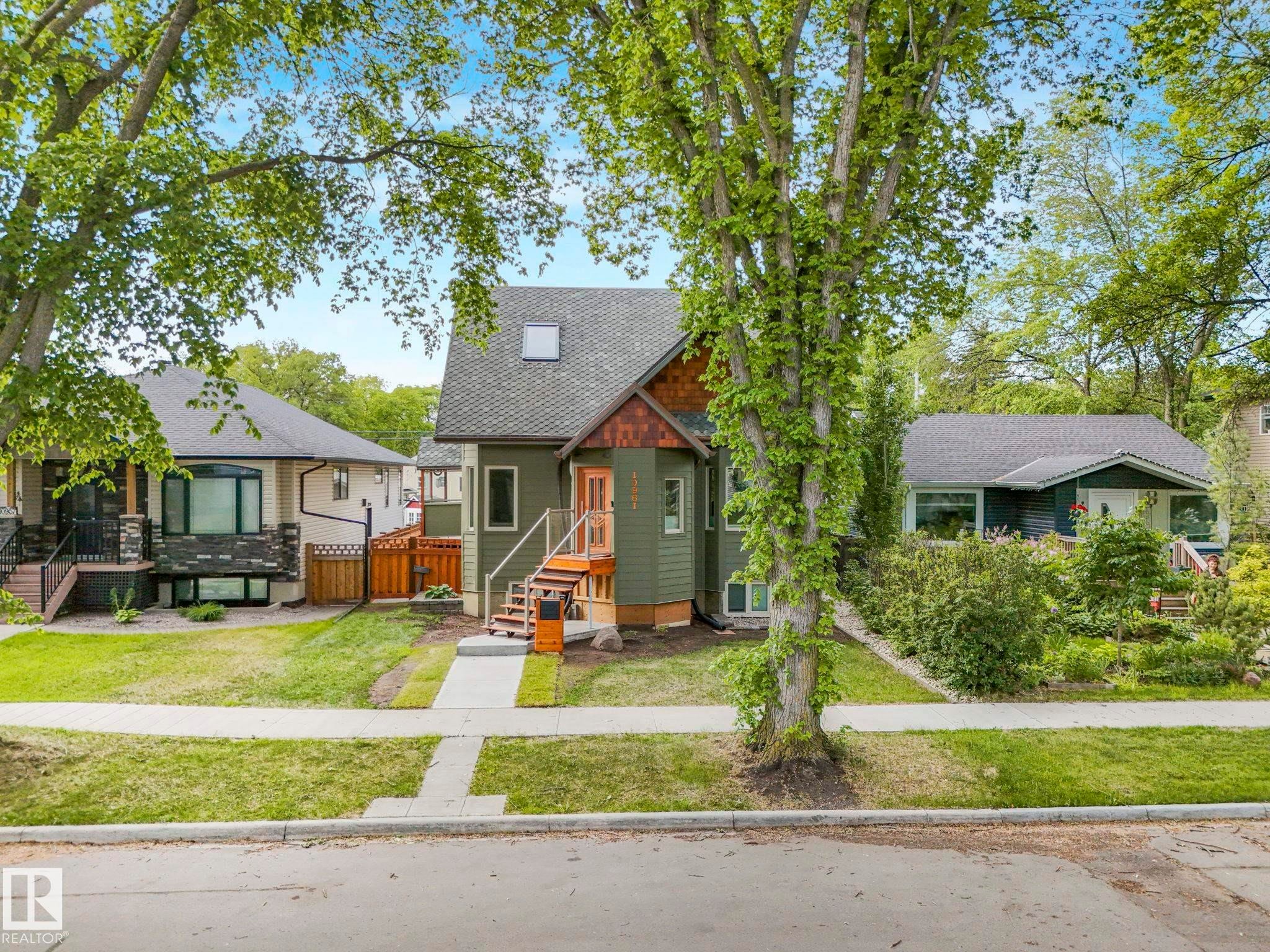 Green-sided residence featuring a gabled roofline, front entryway with wood stairs and railings, and a skylight - 10961 75 Avenue, Edmonton, AB - Outdoor