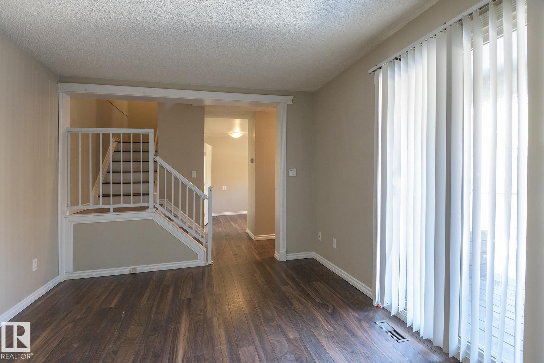 Spacious room featuring wood-finish flooring, a contemporary staircase with white railings, and direct access to an outdoor area via sliding glass doors - 8039 27 Avenue, Edmonton, AB - Indoor Photo Showing Other Room
