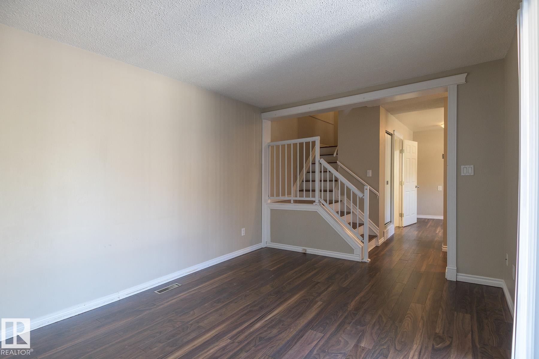 Spacious room featuring wood-finish flooring, neutral-toned walls, and white baseboards - 8039 27 Avenue, Edmonton, AB - Indoor Photo Showing Other Room
