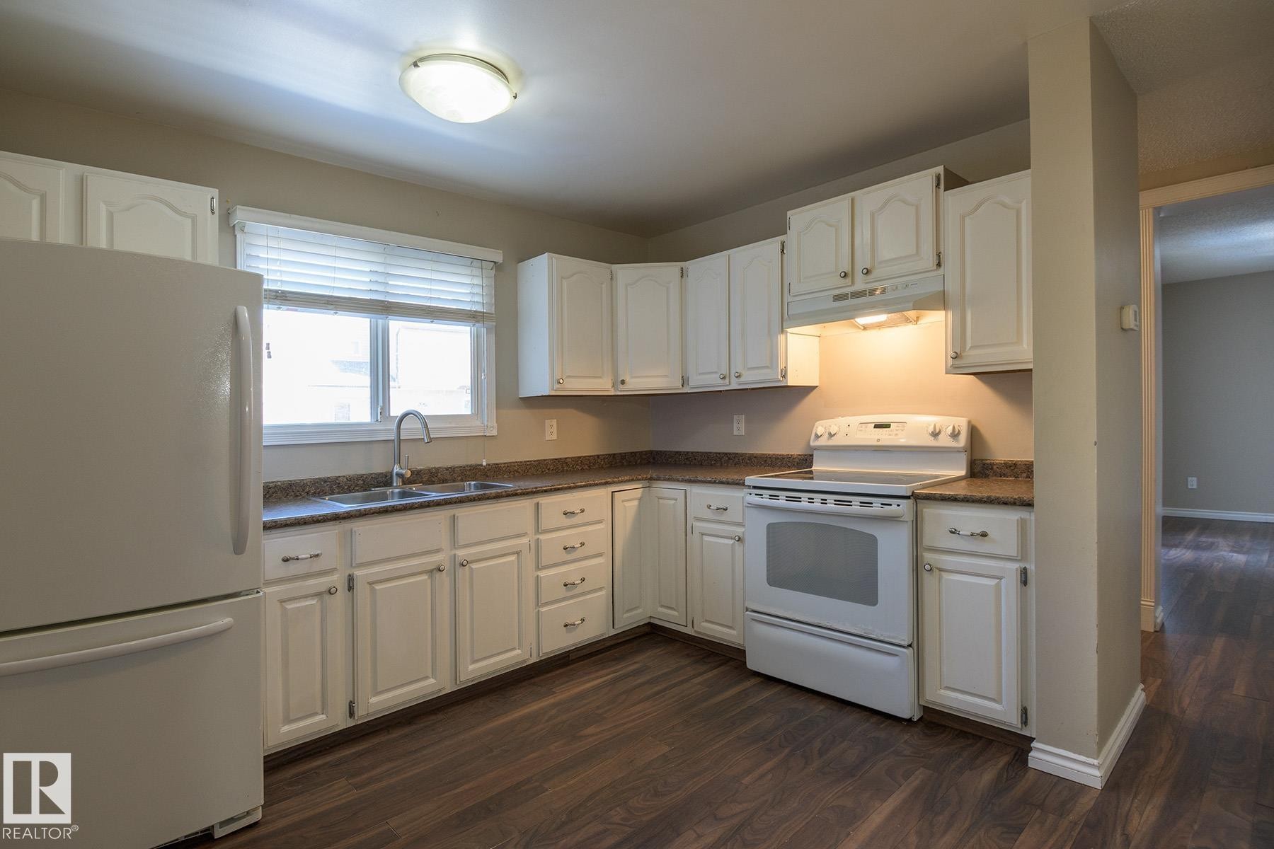 Bright kitchen featuring white cabinetry, dark speckled countertops, a double basin sink with a high-arc faucet, and wood-finish flooring - 8039 27 Avenue, Edmonton, AB - Indoor Photo Showing Kitchen With Double Sink