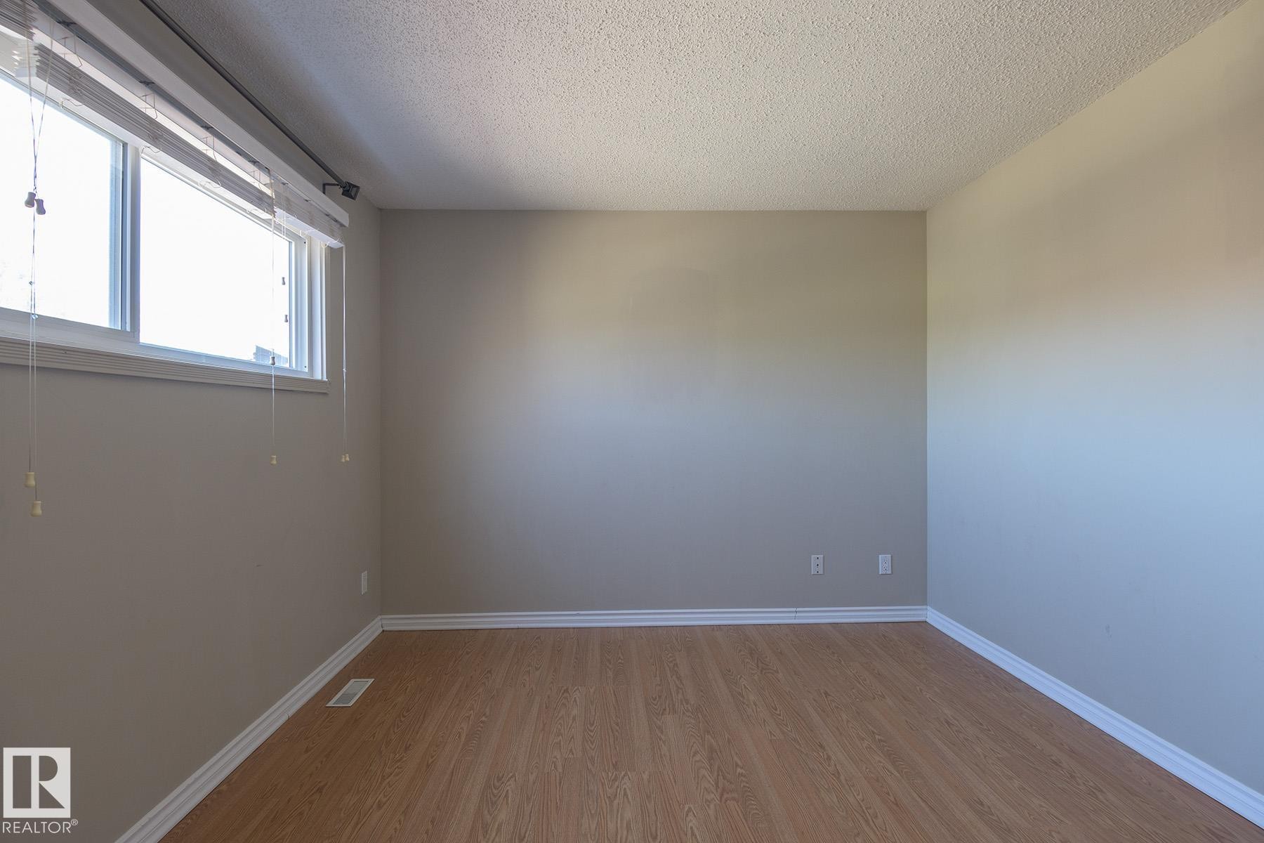 Spacious room featuring wood-finish flooring, neutral-toned walls, white baseboards, and a window with blinds - 8039 27 Avenue, Edmonton, AB - Indoor Photo Showing Other Room