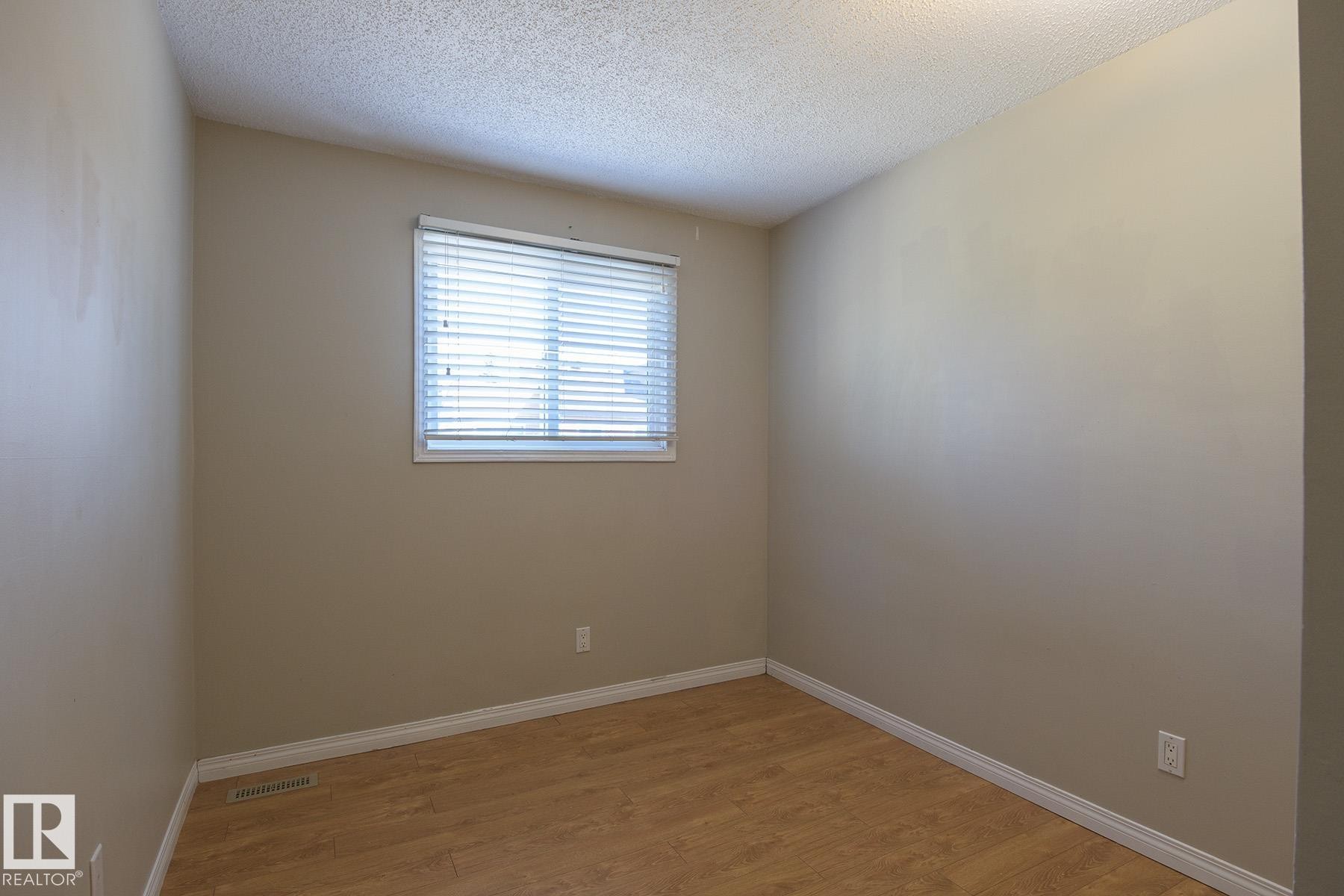 Room featuring a single window with blinds, neutral painted walls, wood-finish flooring, white baseboards, and a textured ceiling - 8039 27 Avenue, Edmonton, AB - Indoor Photo Showing Other Room