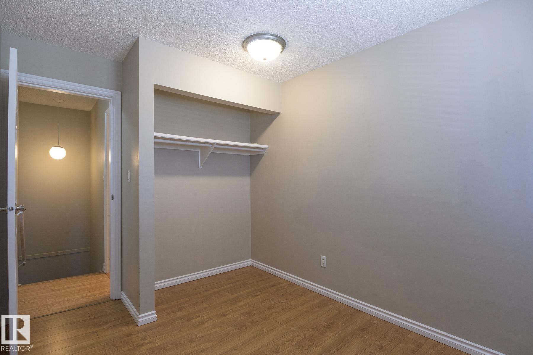 Room featuring wood-finish flooring, light grey painted walls, white trim, and a built-in closet with shelving and a hanging rod - 8039 27 Avenue, Edmonton, AB - Indoor Photo Showing Other Room