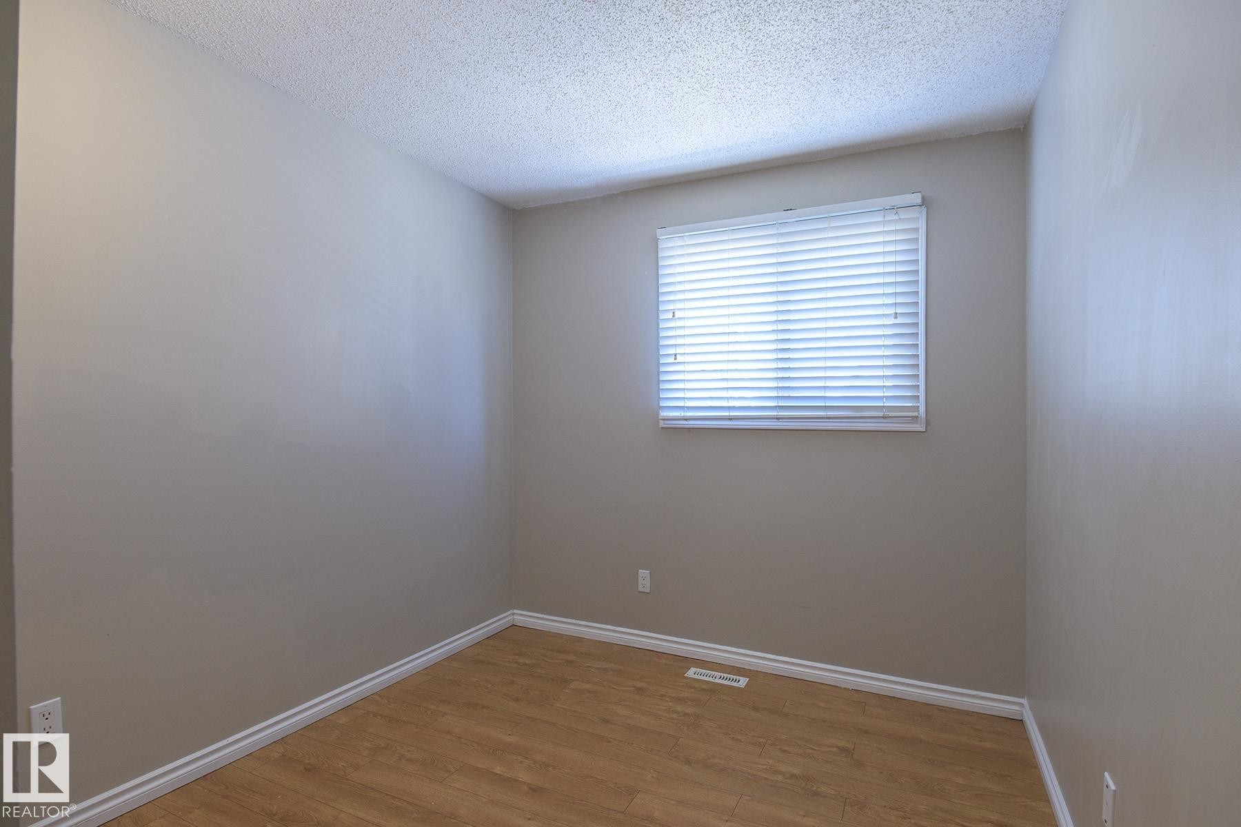 Spacious room with light-toned walls, wood-finish flooring, and white baseboards - 8039 27 Avenue, Edmonton, AB - Indoor Photo Showing Other Room