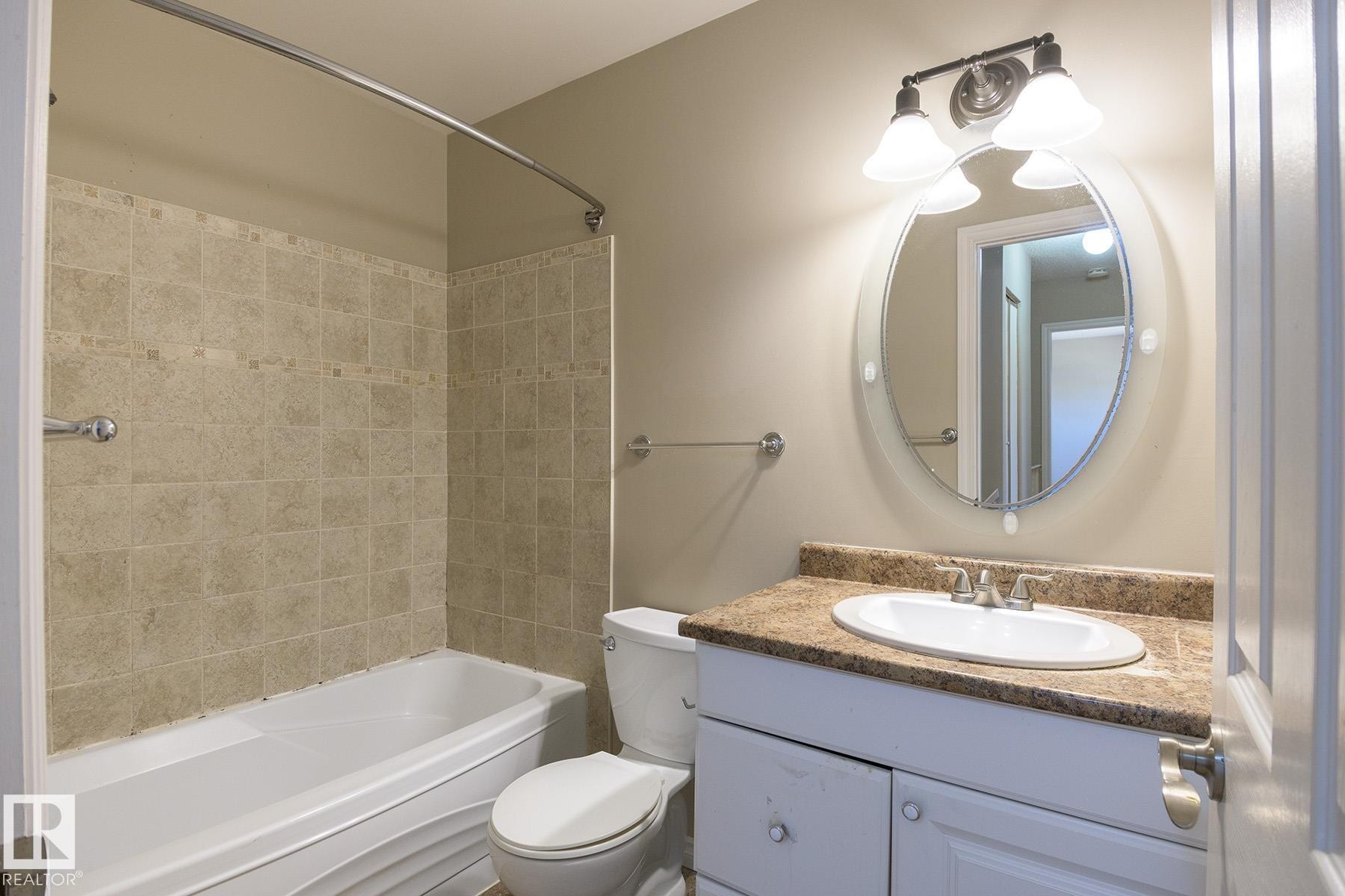 Bathroom featuring a white bathtub with tile surround, white vanity with an integrated sink, patterned countertop, and an oval mirror with an overhead light fixture - 8039 27 Avenue, Edmonton, AB - Indoor Photo Showing Bathroom