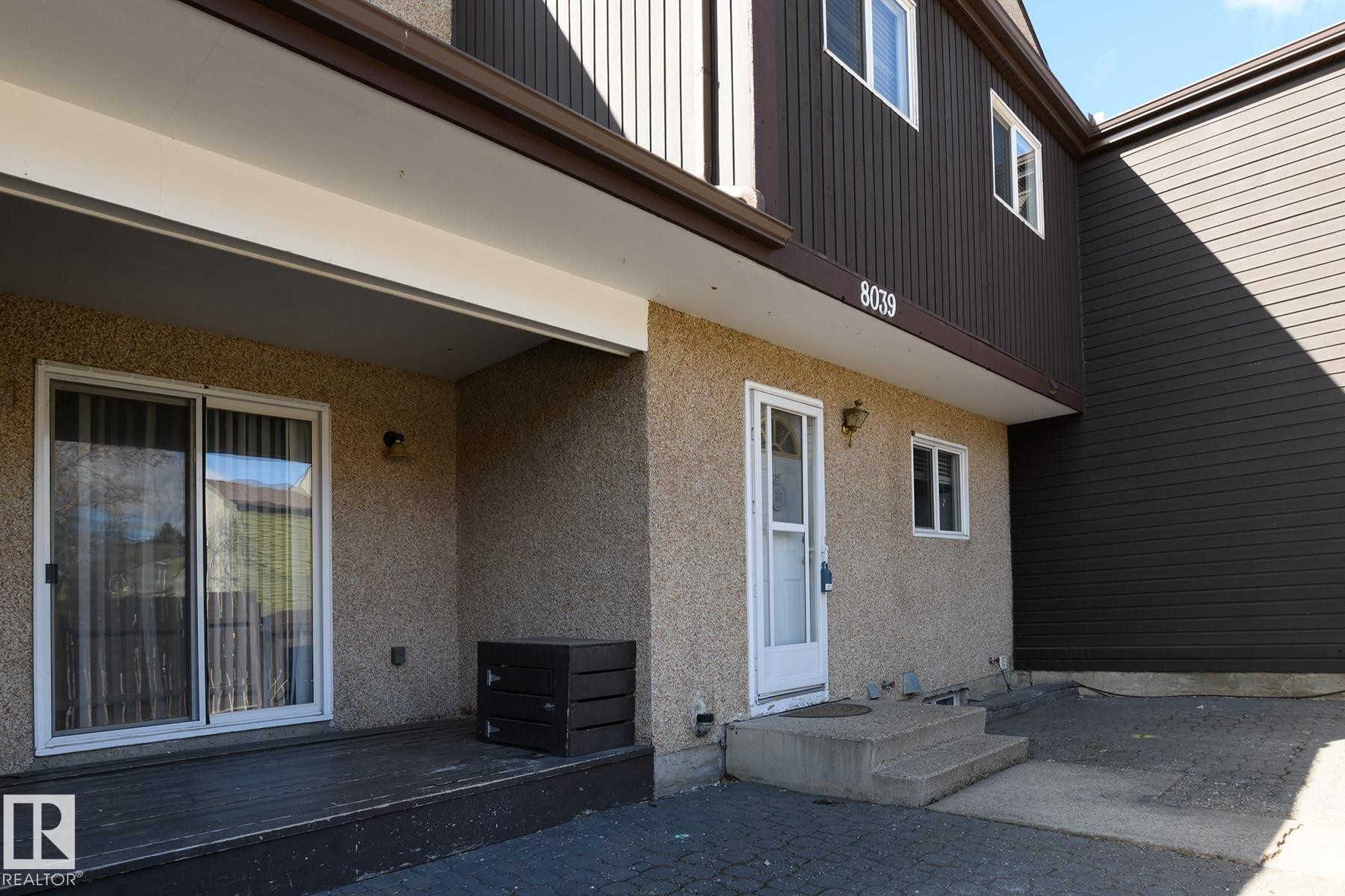 Ground-level patio with sliding glass doors, textured stucco exterior, and a secondary entry door - 8039 27 Avenue, Edmonton, AB - Outdoor With Exterior