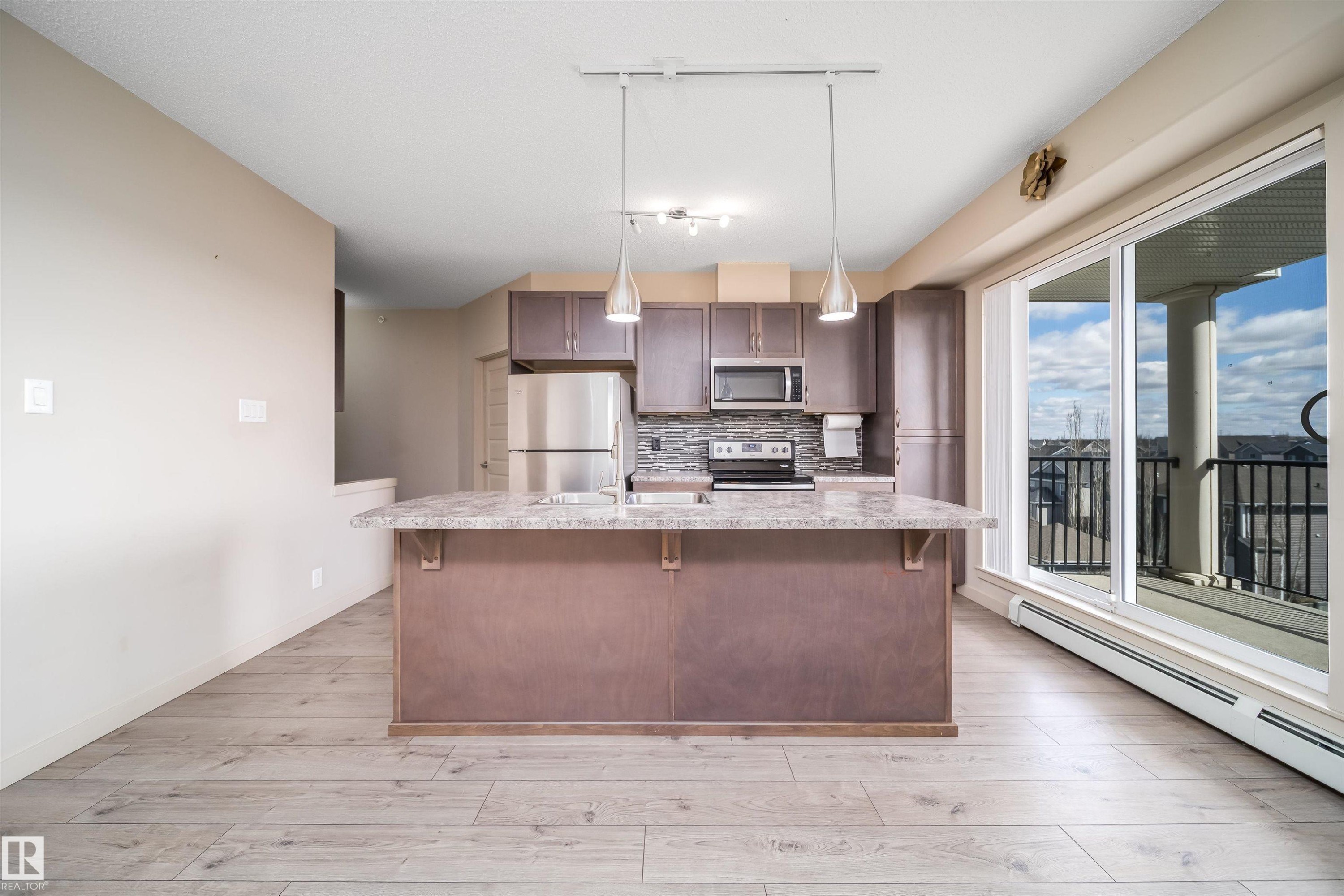 Contemporary kitchen with wood-finish flooring and a central island featuring a light-toned countertop - 421 4008 Savaryn Drive, Edmonton, AB - Indoor Photo Showing Kitchen With Upgraded Kitchen
