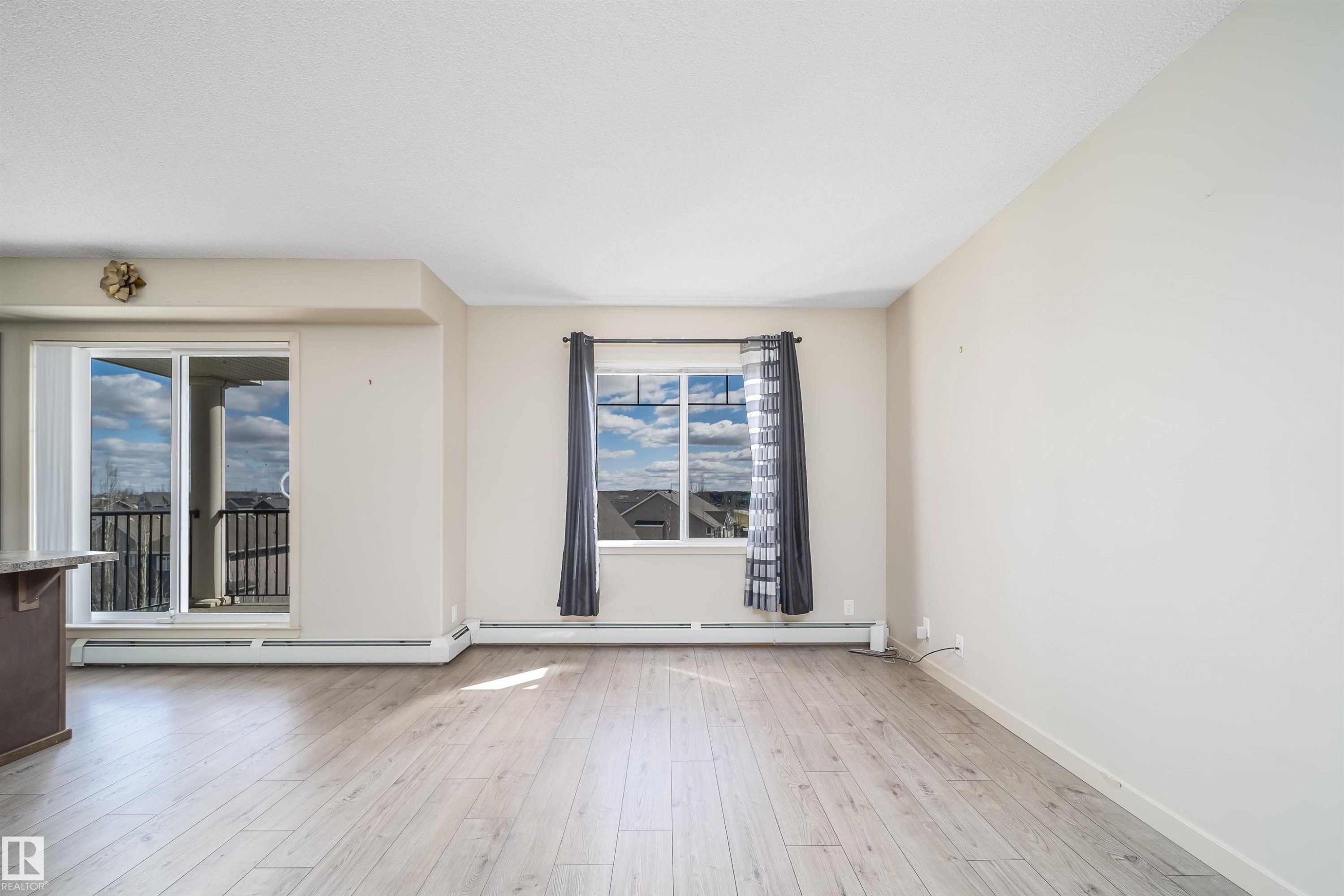 Spacious open-concept room featuring light wood-finish flooring, neutral wall tones, and overhead textured ceilings - 421 4008 Savaryn Drive, Edmonton, AB - Indoor