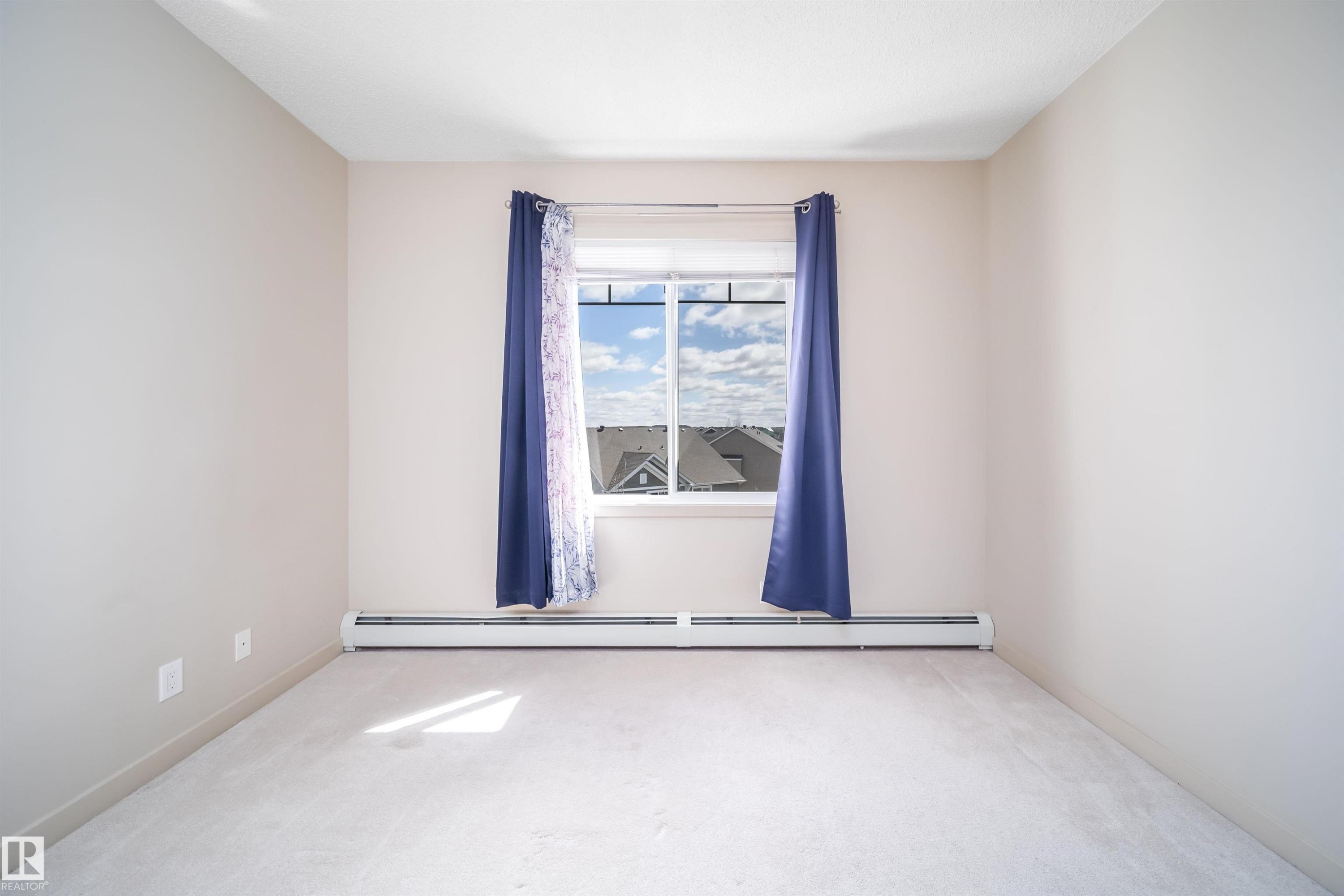 Bedroom featuring a window with white trim, light-colored carpeting, baseboard heating, and neutral painted walls - 421 4008 Savaryn Drive, Edmonton, AB - Indoor Photo Showing Other Room