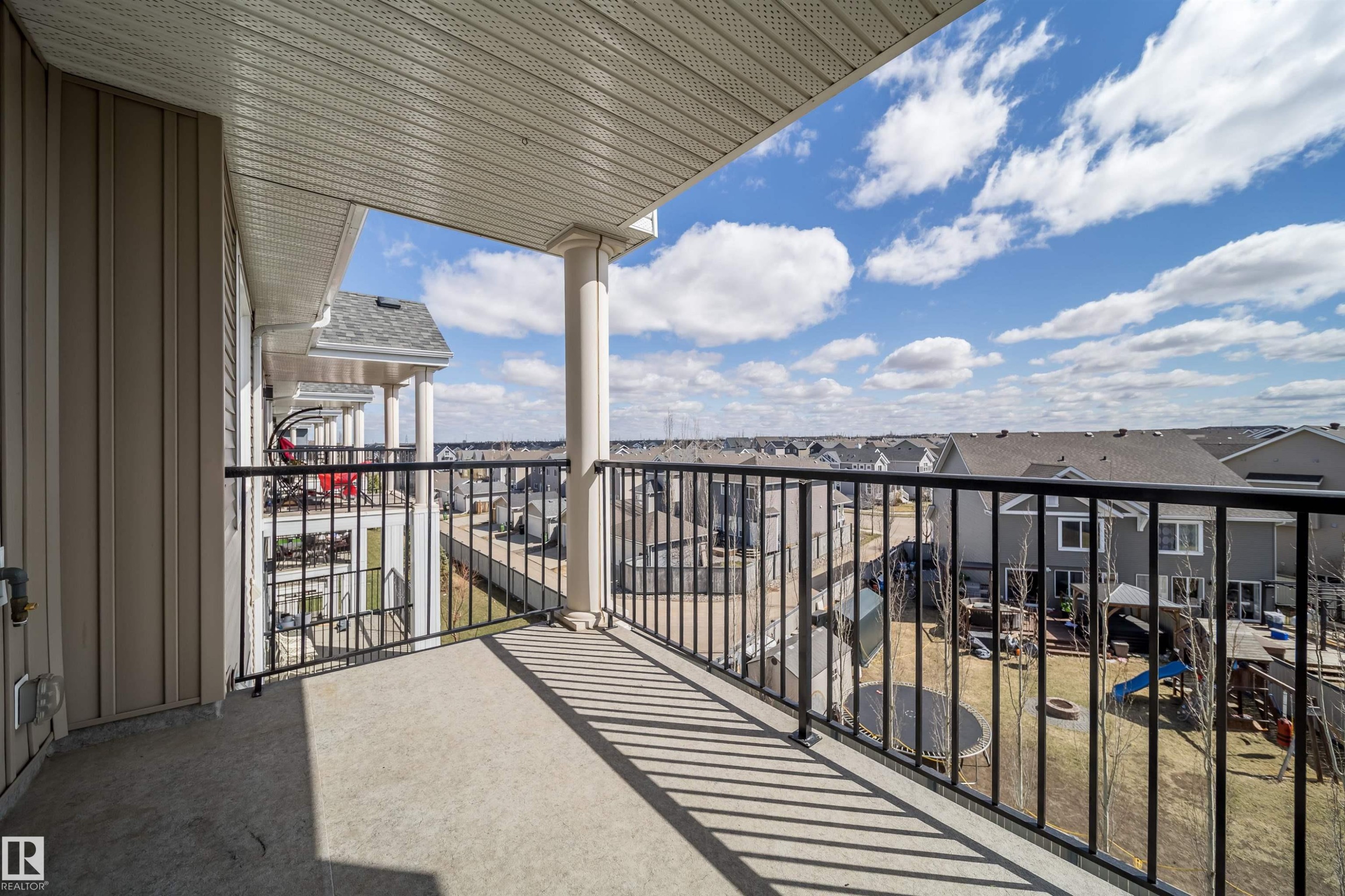 Exterior balcony featuring concrete flooring, a black metal railing, a prominent support column, and beige vertical siding - 421 4008 Savaryn Drive, Edmonton, AB - Outdoor With View With Exterior