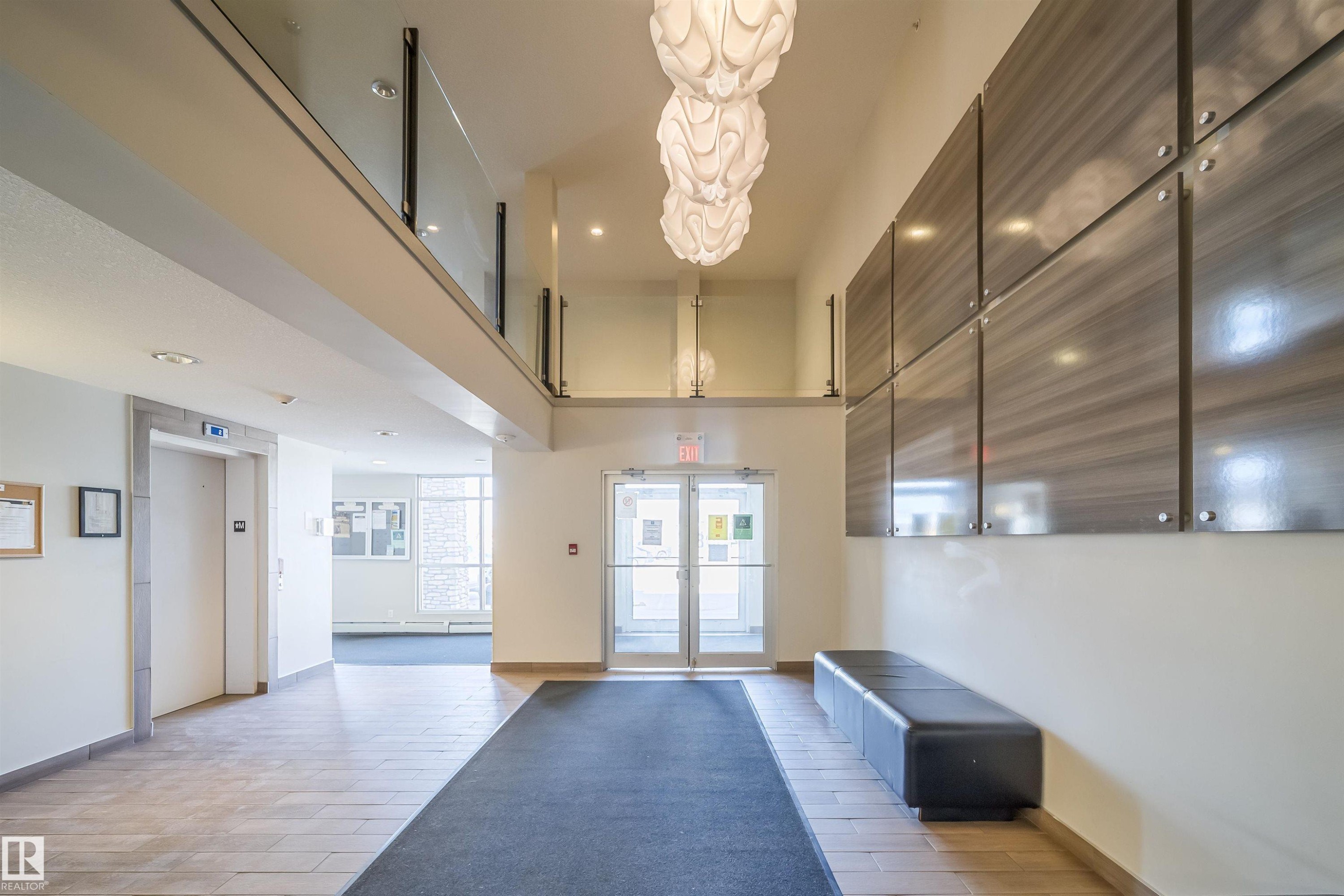 Lobby area featuring large format tile flooring, three decorative pendant light fixtures, and a glass-paneled upper-level railing - 421 4008 Savaryn Drive, Edmonton, AB - Indoor Photo Showing Other Room
