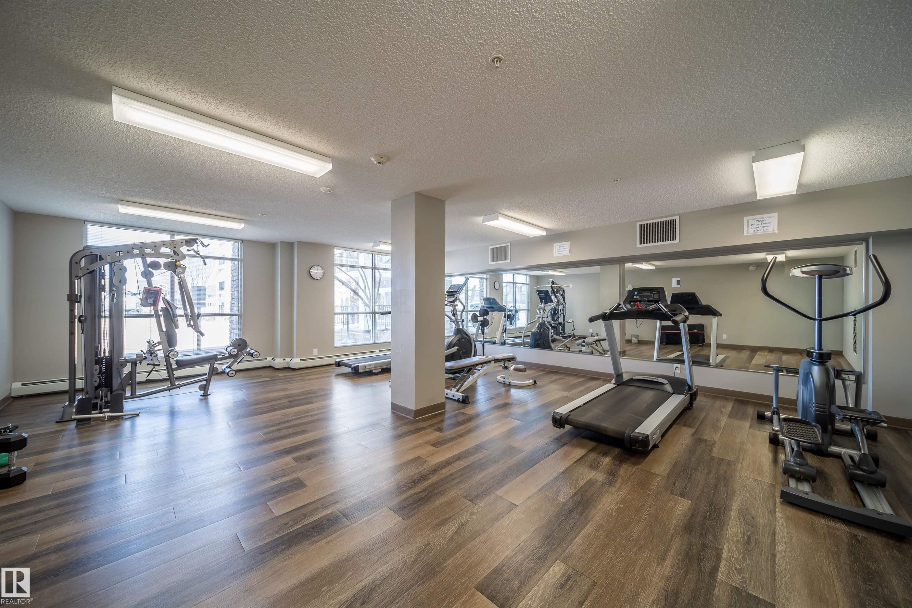 Fitness center featuring wood-finish flooring, a full-wall mirror, and ample natural light from multiple windows - 421 4008 Savaryn Drive, Edmonton, AB - Indoor Photo Showing Gym Room