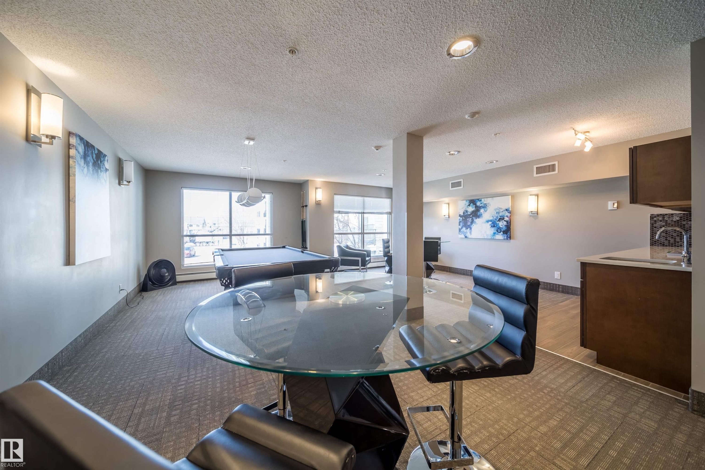 Spacious common area featuring patterned carpet flooring, extensive window placements, recessed lighting, and a built-in wet bar with a tile backsplash - 421 4008 Savaryn Drive, Edmonton, AB - Indoor