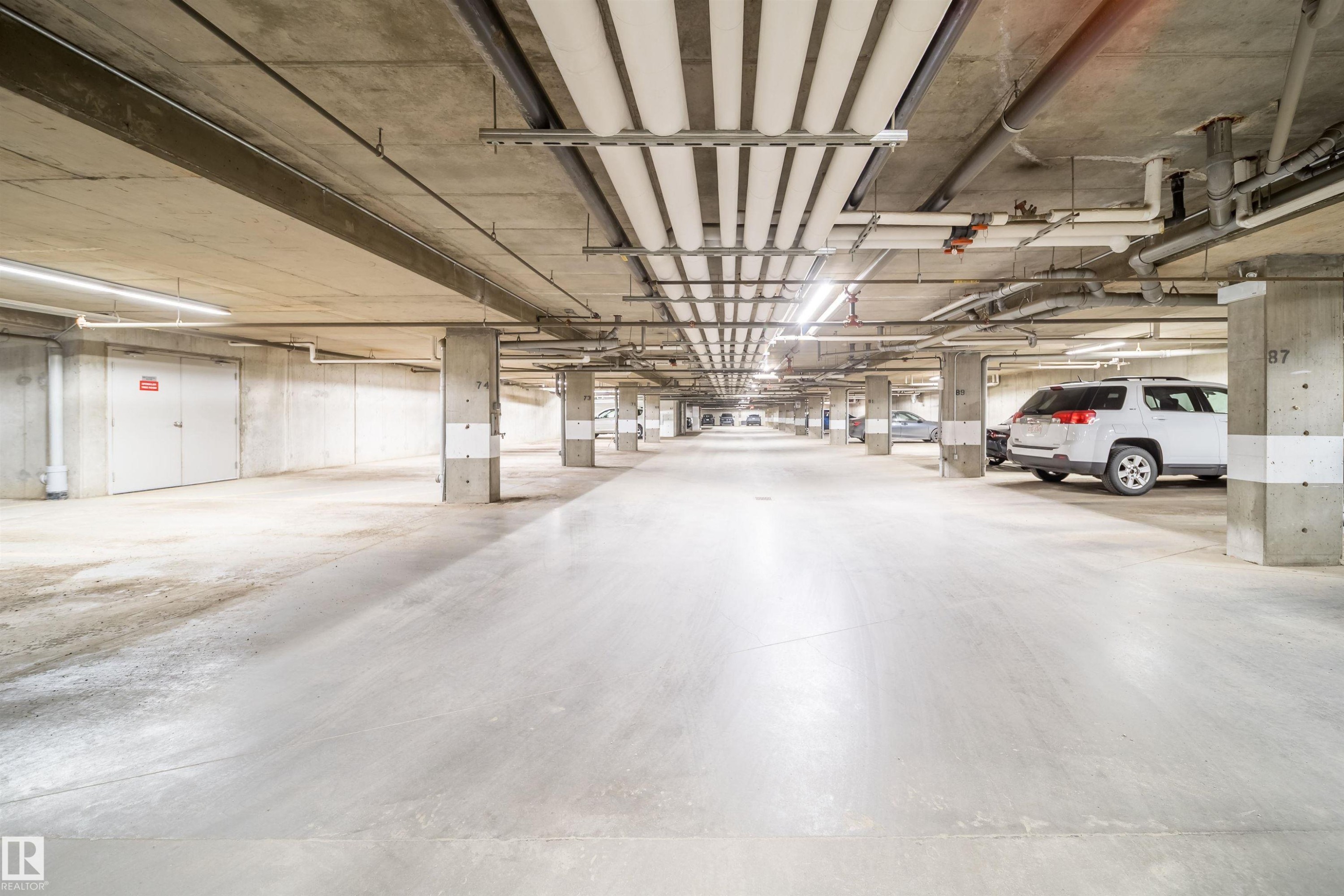 Spacious underground parking facility with concrete flooring, exposed concrete ceilings, and ample overhead lighting - 421 4008 Savaryn Drive, Edmonton, AB - Indoor Photo Showing Garage