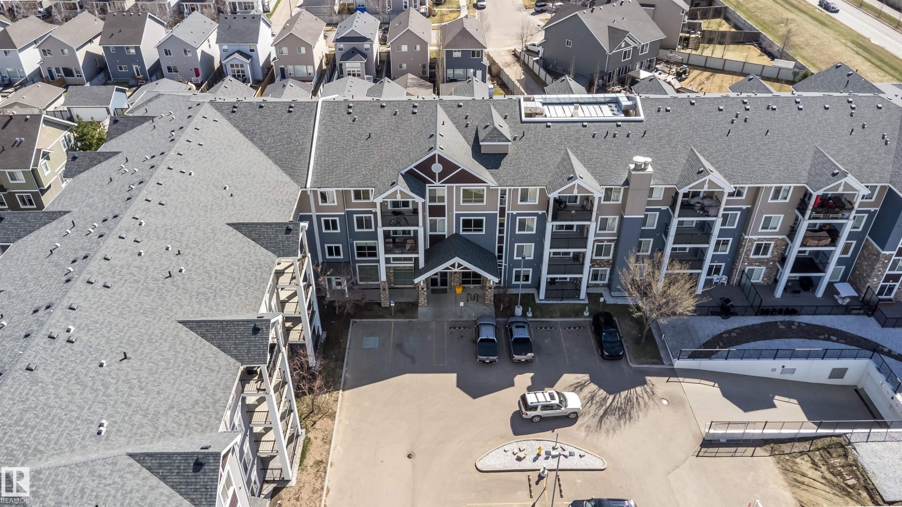 Multi-level residential building featuring a dark gray shingle roof, multiple private balconies, a stone-clad facade, and a dedicated parking area - 421 4008 Savaryn Drive, Edmonton, AB - With Facade