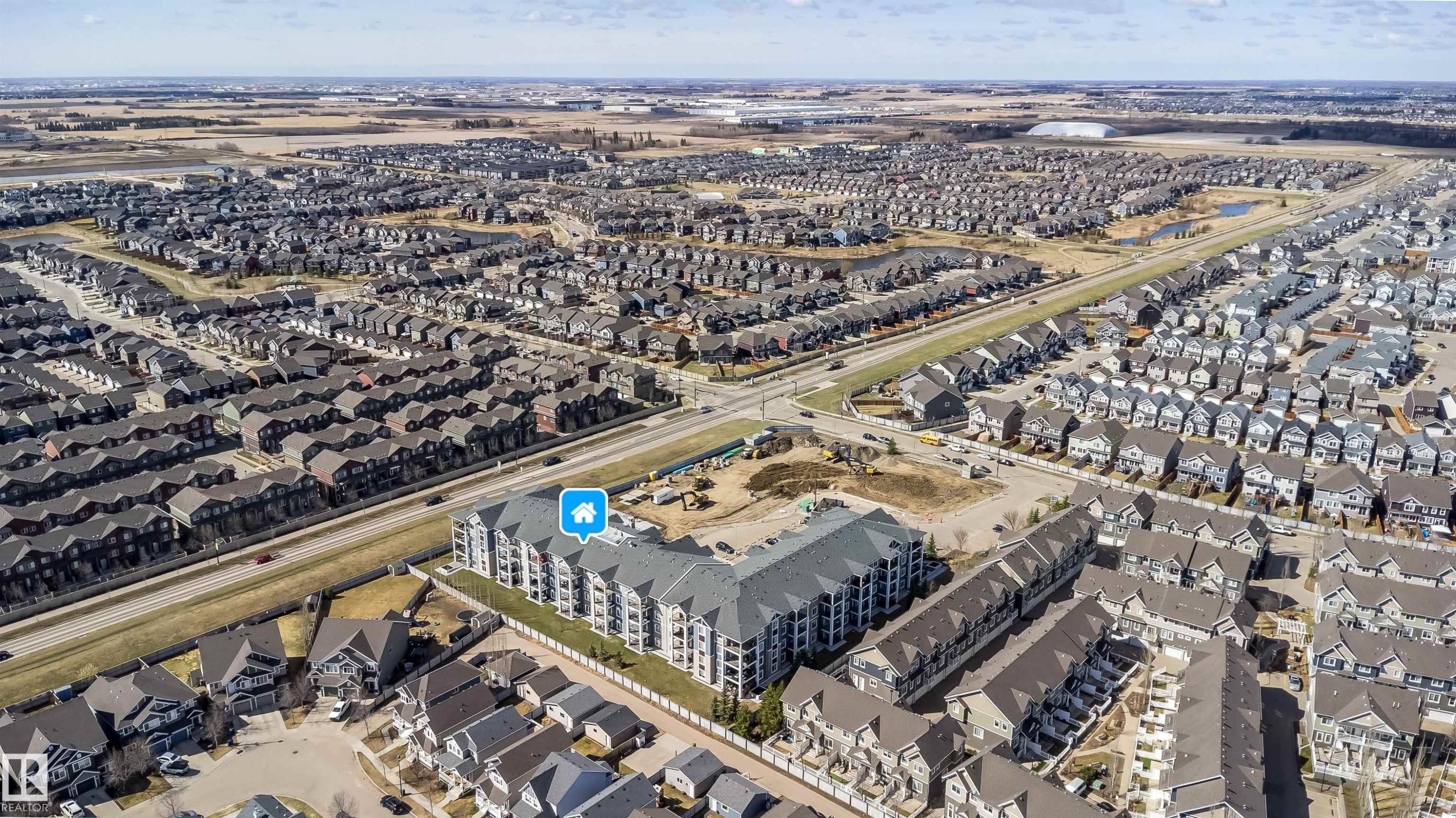 Contemporary multi-story building featuring light-toned exterior siding, a dark pitched roofline, multiple balconies, and visible surface parking - 421 4008 Savaryn Drive, Edmonton, AB - Outdoor With View